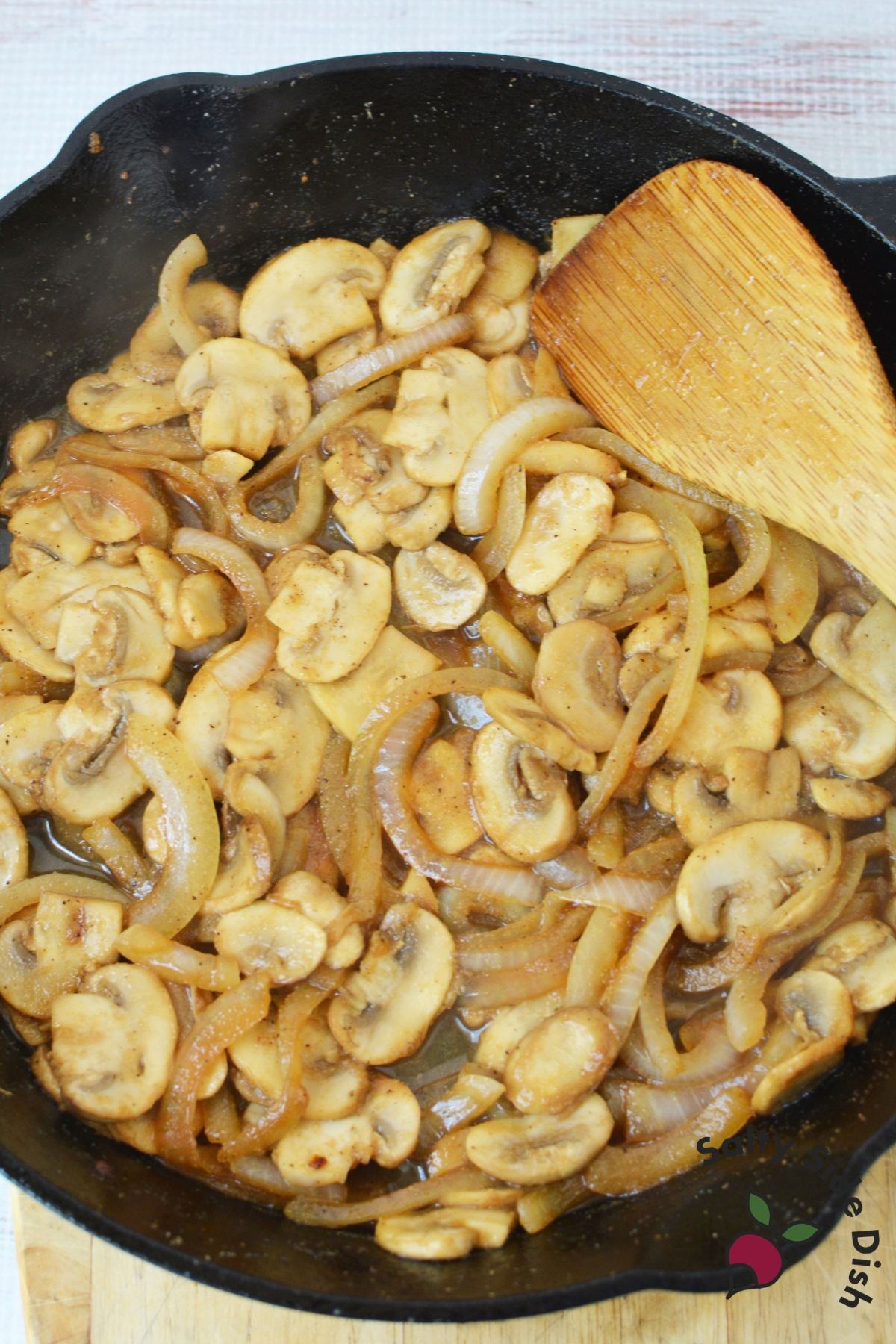 sliced mushrooms and chicken in a cast iron pan being stirred.