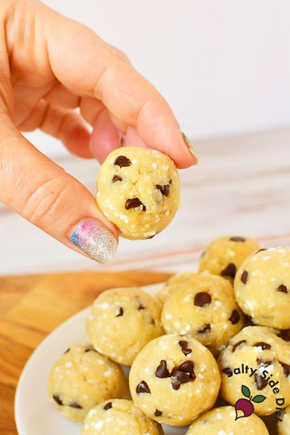 hand holding a cottage cheese cookie dough ball above a plate of cookie dough bites