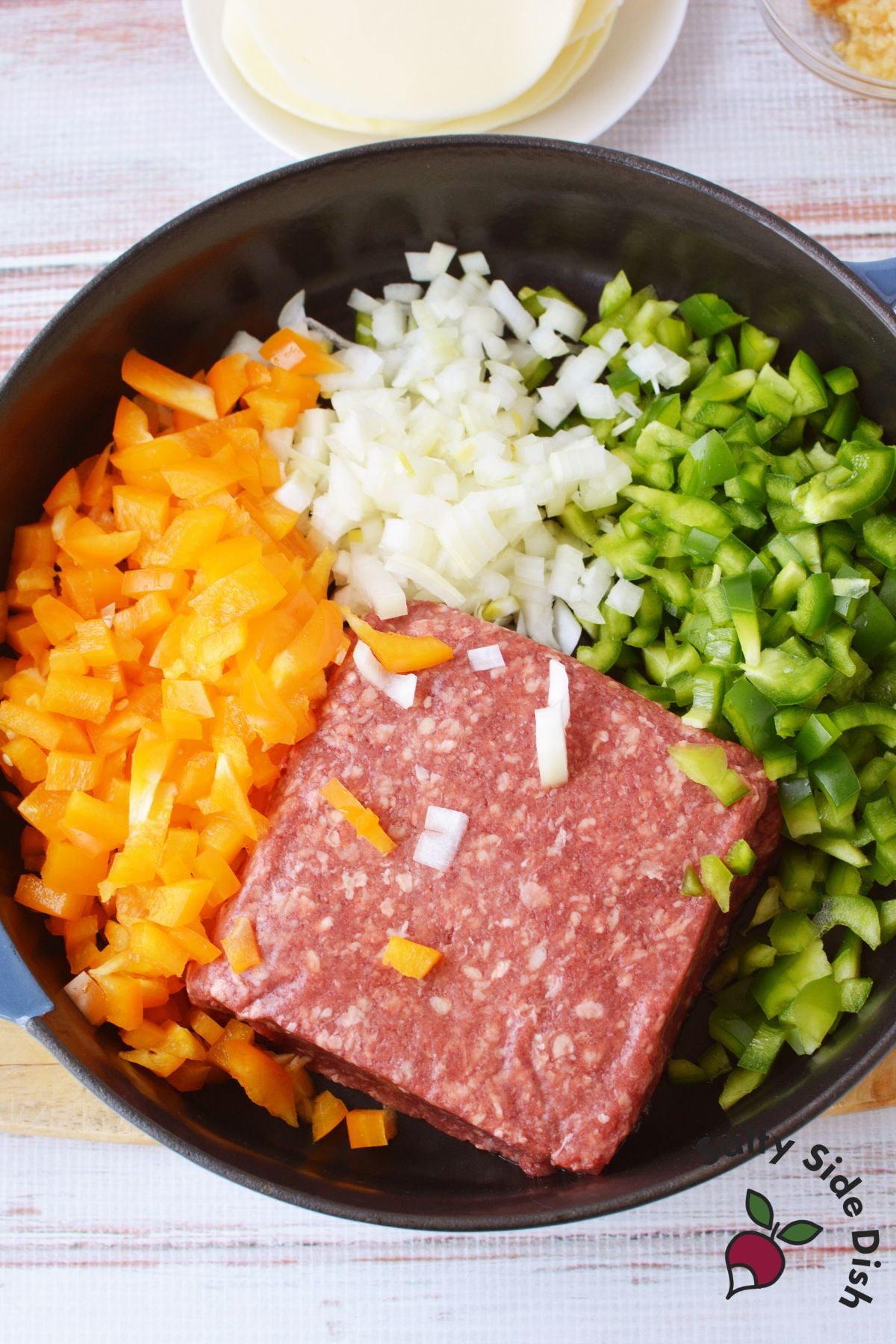 Raw ground beef, diced orange pepper, onion, and green pepper in a cast iron skillet before cooking