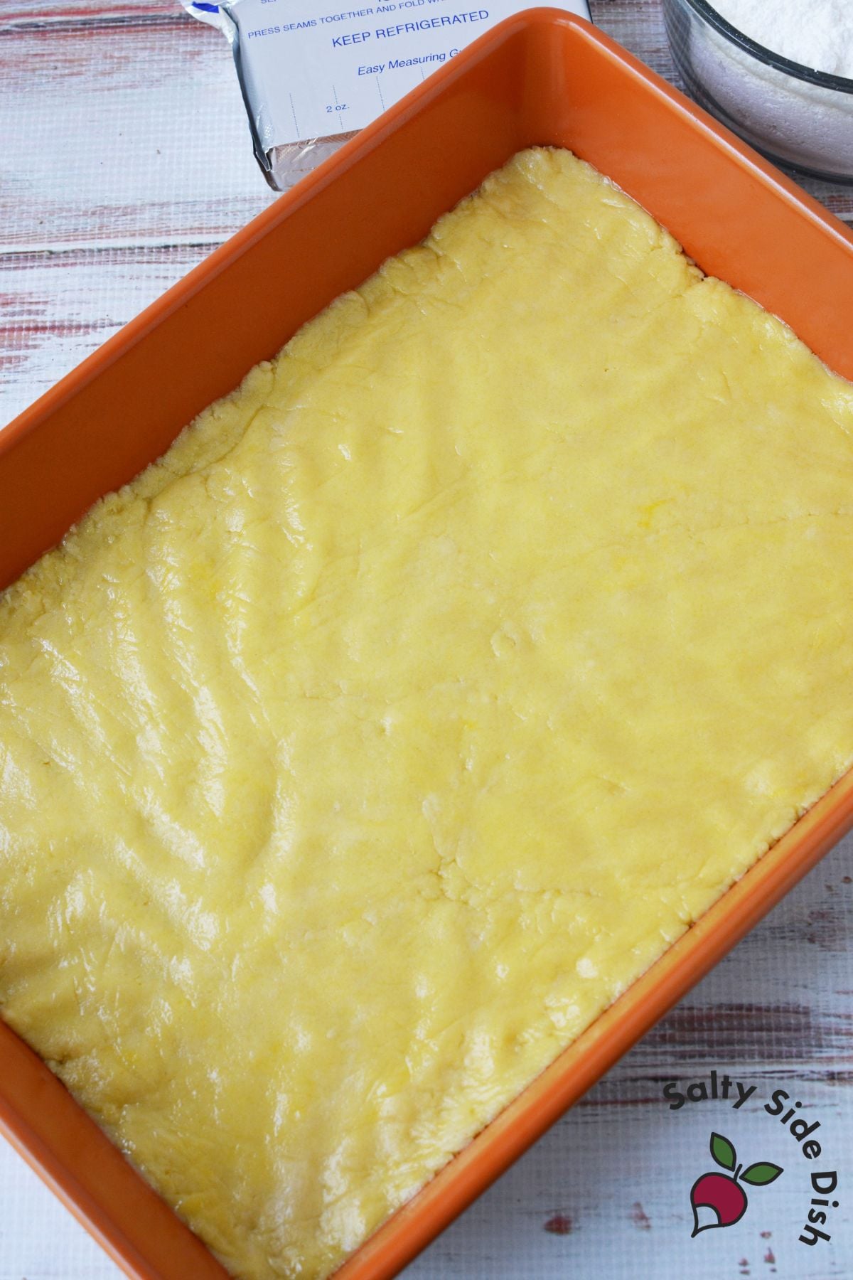 Lemon cookie bar crust pressed evenly into a baking dish before baking