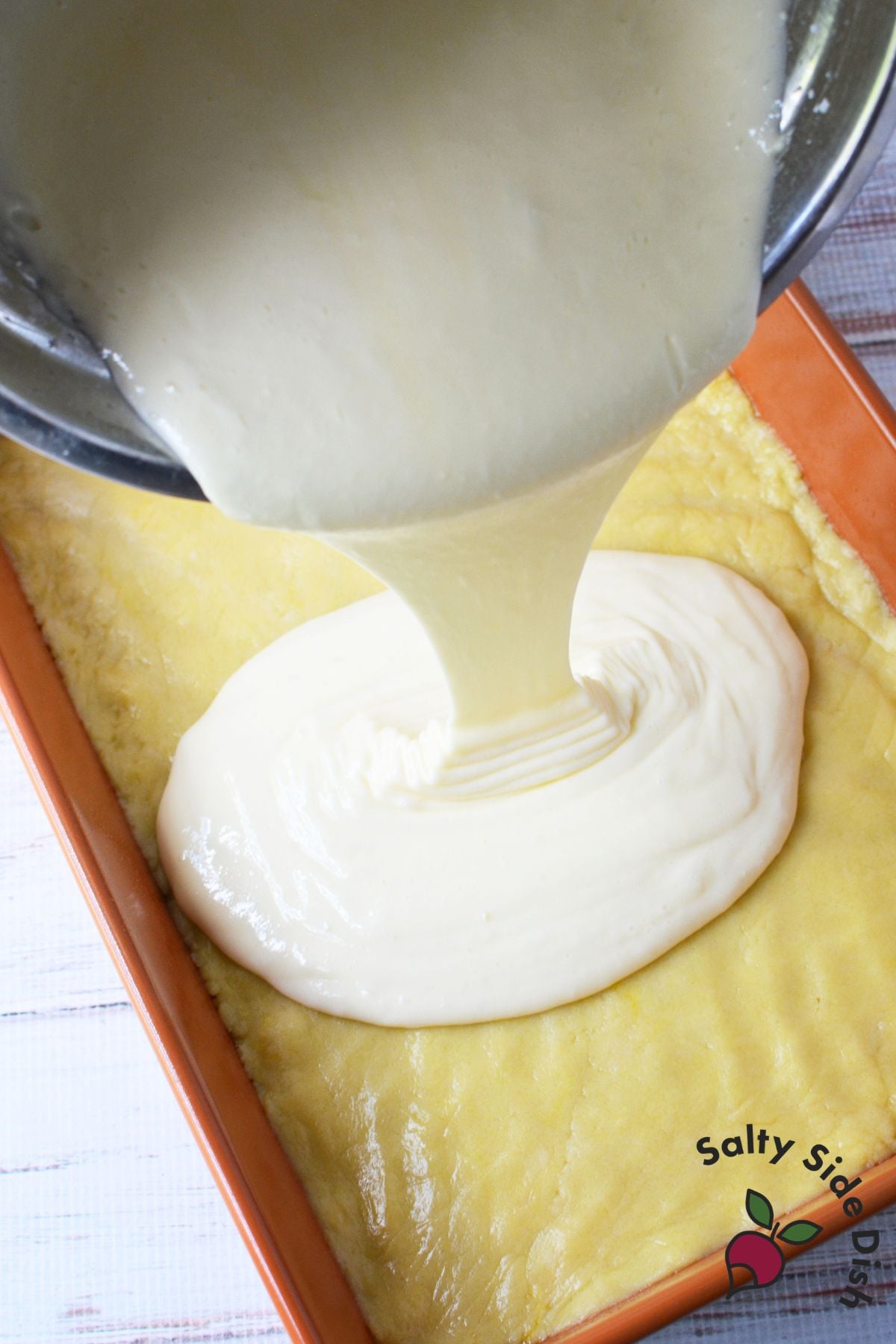 Cream cheese filling being poured over lemon cookie crust in a baking pan