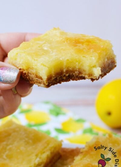 Hand holding a homemade lemon cookie bar with creamy lemon filling