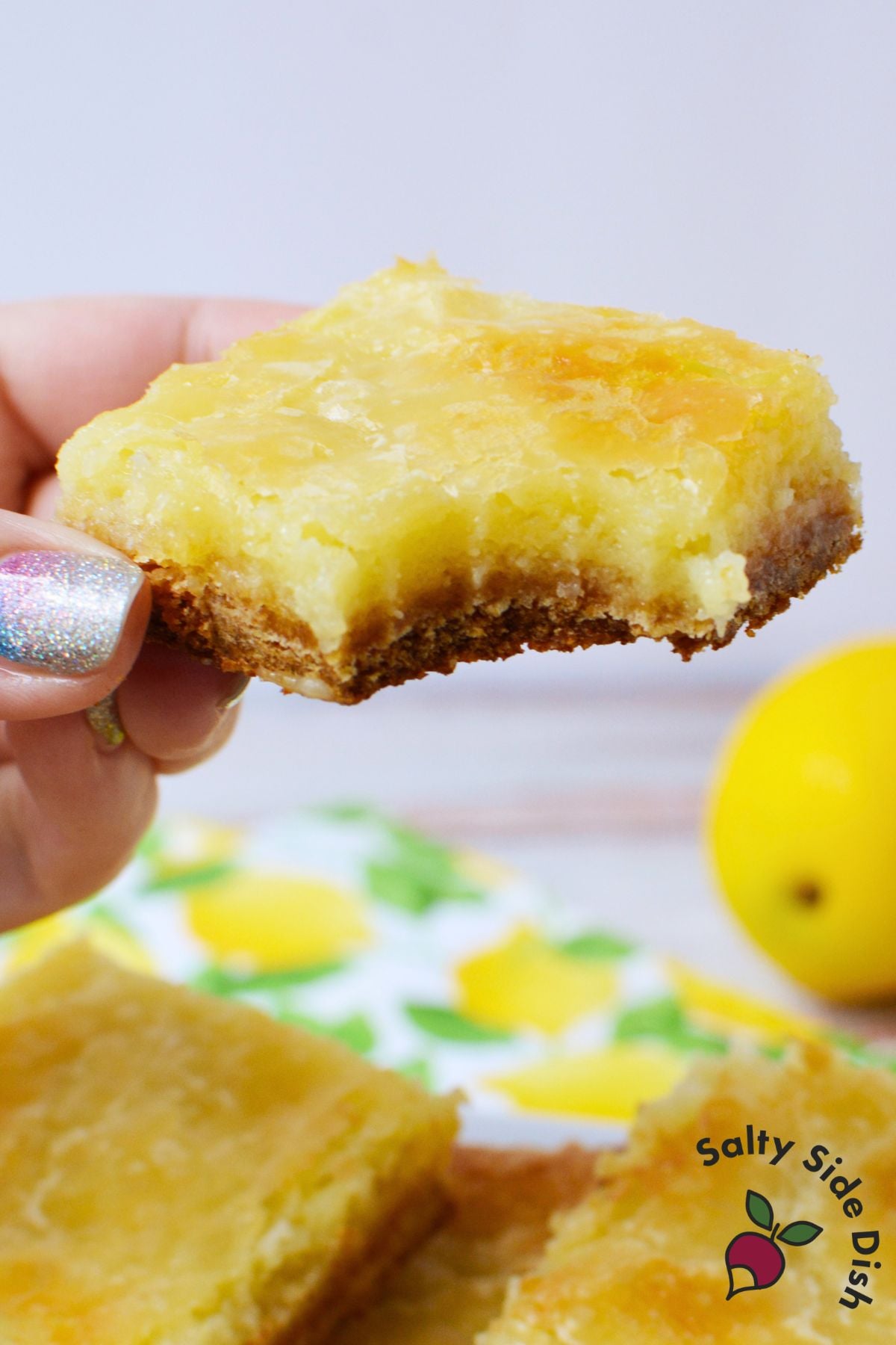 Hand holding a homemade lemon cookie bar with creamy lemon filling
