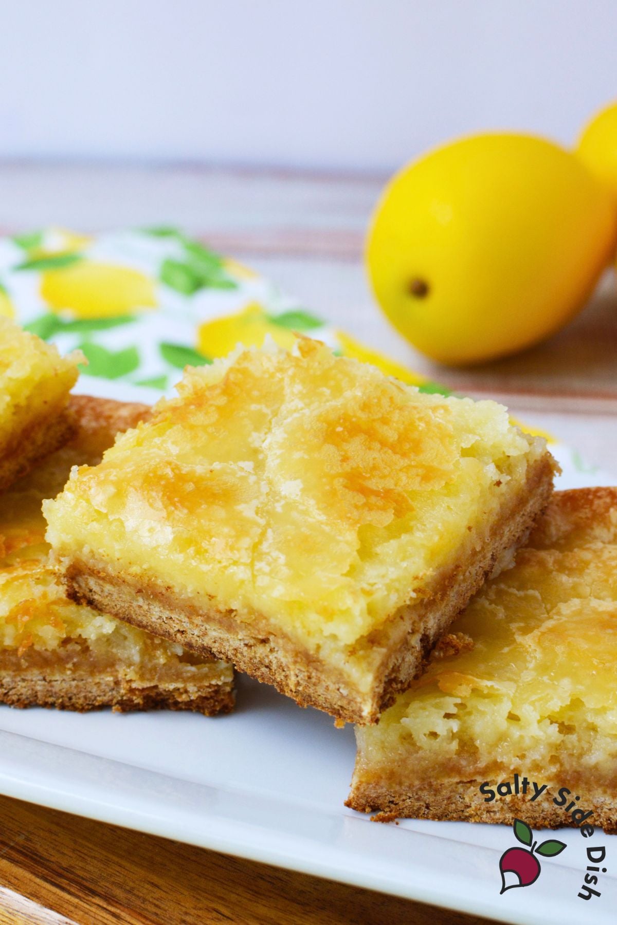 Stack of homemade lemon cookie bars on a serving plate with fresh lemons in the background