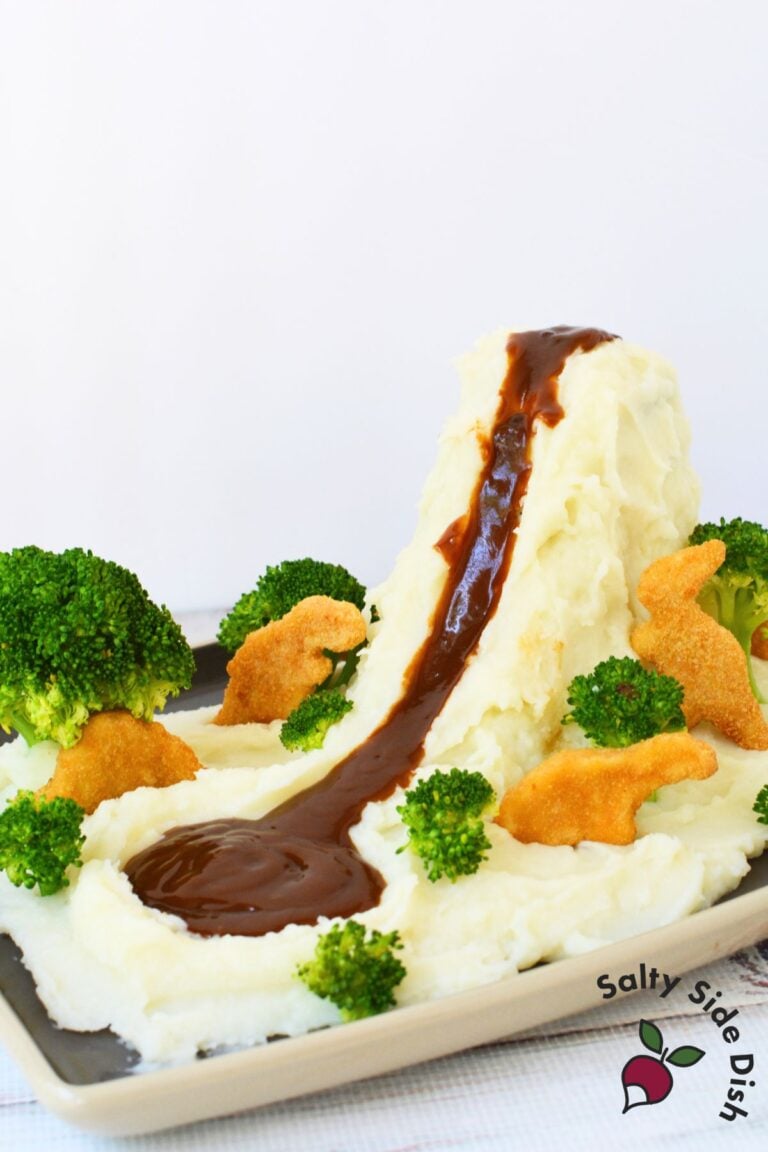 Mashed potato volcano with brown gravy flowing down into a lake surrounded by broccoli and dino nuggets