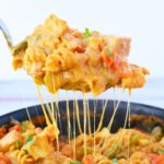 Spoonful of one pan fajita chicken pasta lifted from the skillet with a melted cheese pull