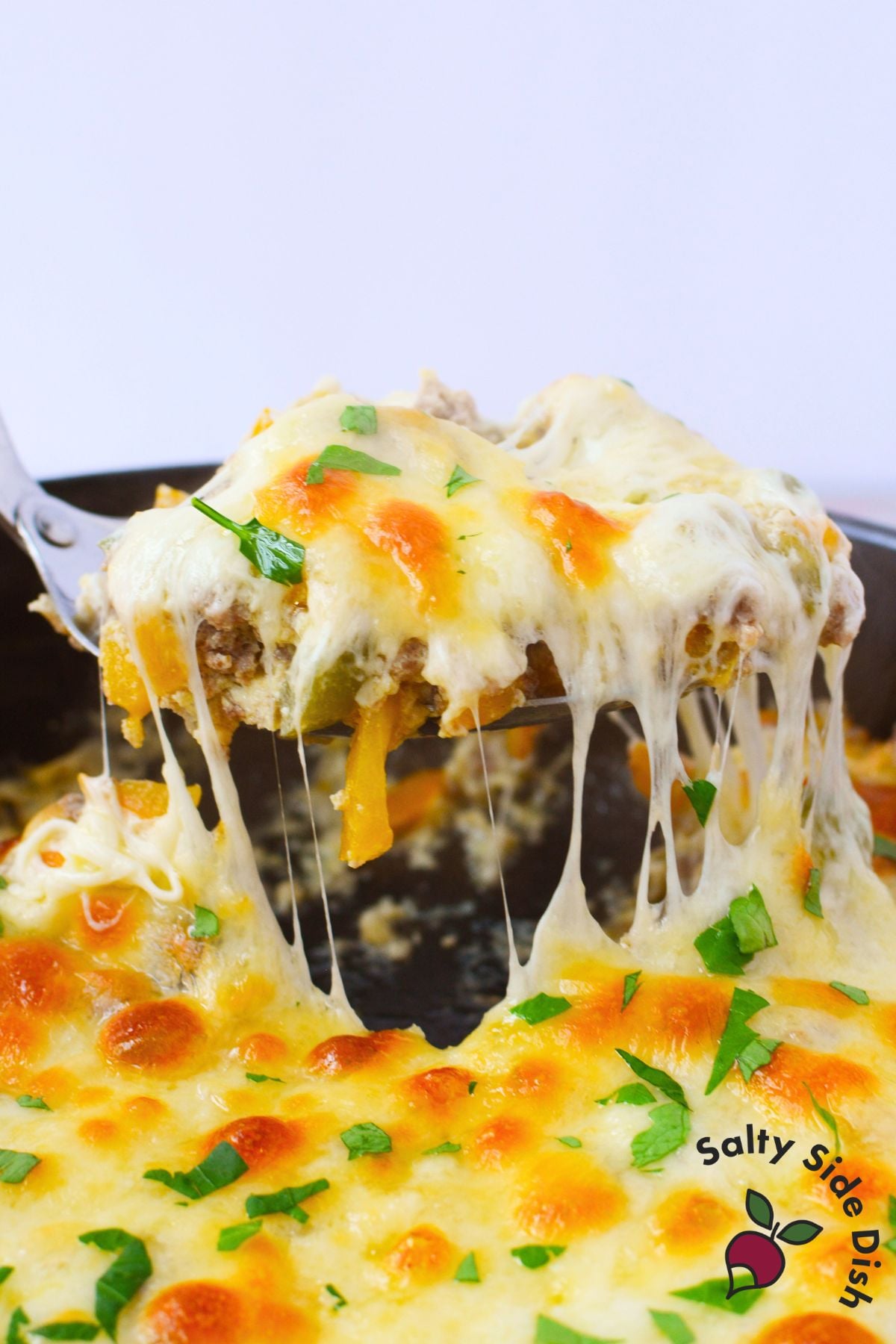 Spoonful of philly cheesesteak casserole lifted from the skillet with a stretchy cheese pull