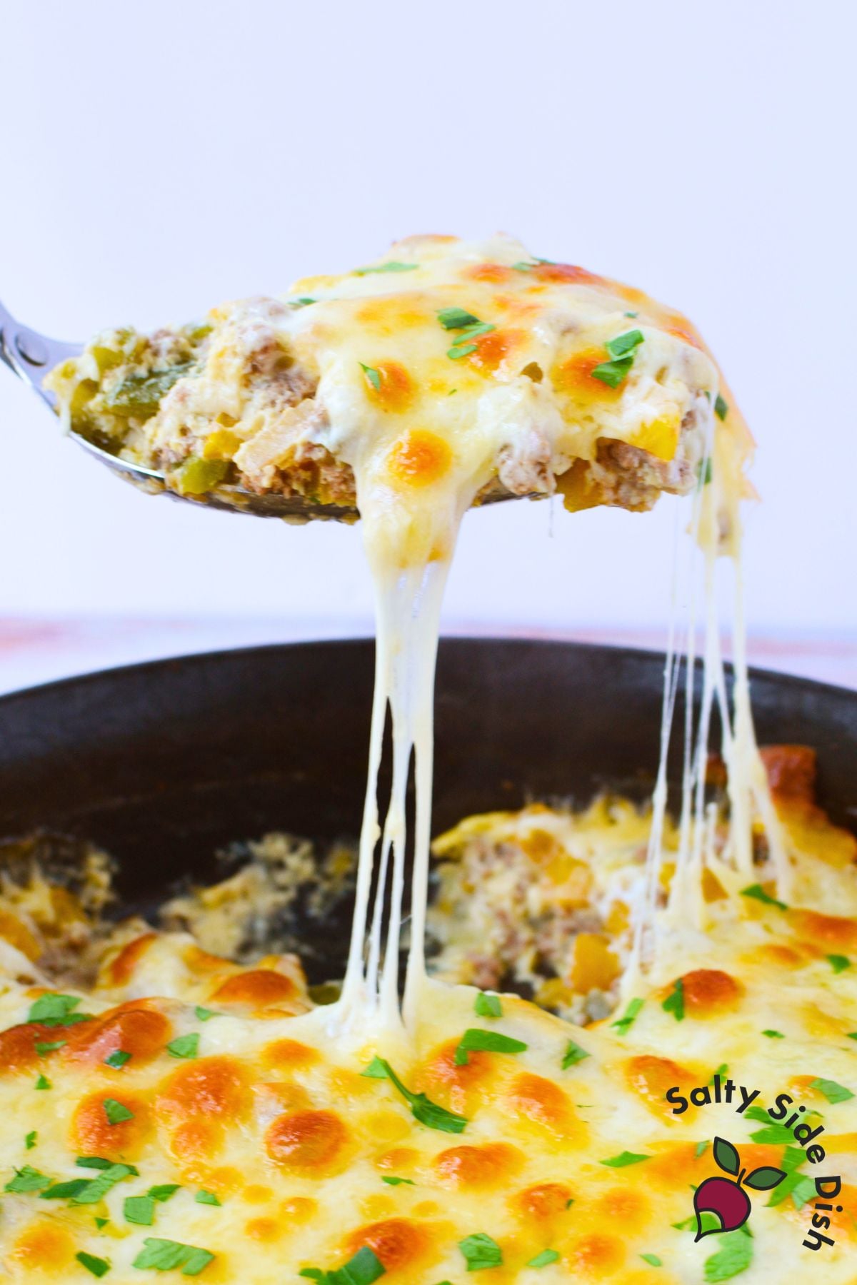 Spoon lifting a cheesy serving of philly cheesesteak casserole from the skillet