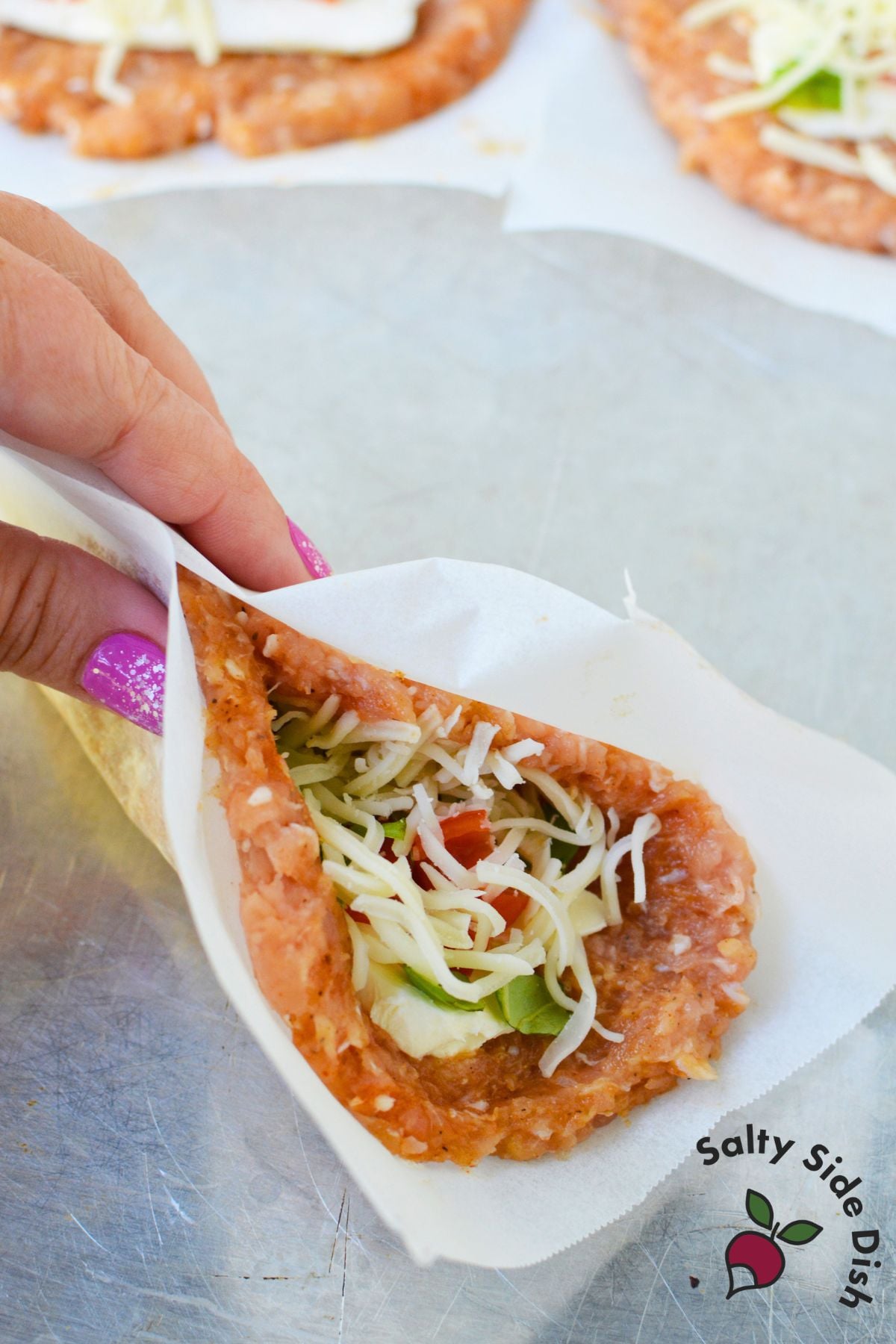 Hand folding a ground chicken patty around cream cheese, tomato, basil, and shredded cheese filling