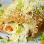 Sliced baked chicken pocket on a white plate showing cream cheese, tomato, and basil filling with a parmesan panko crust