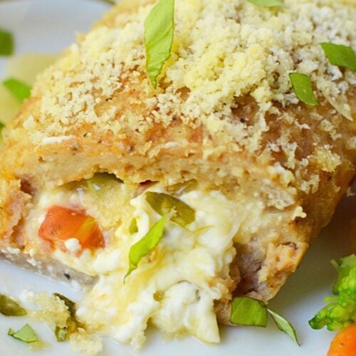 Sliced baked chicken pocket on a white plate showing cream cheese, tomato, and basil filling with a parmesan panko crust