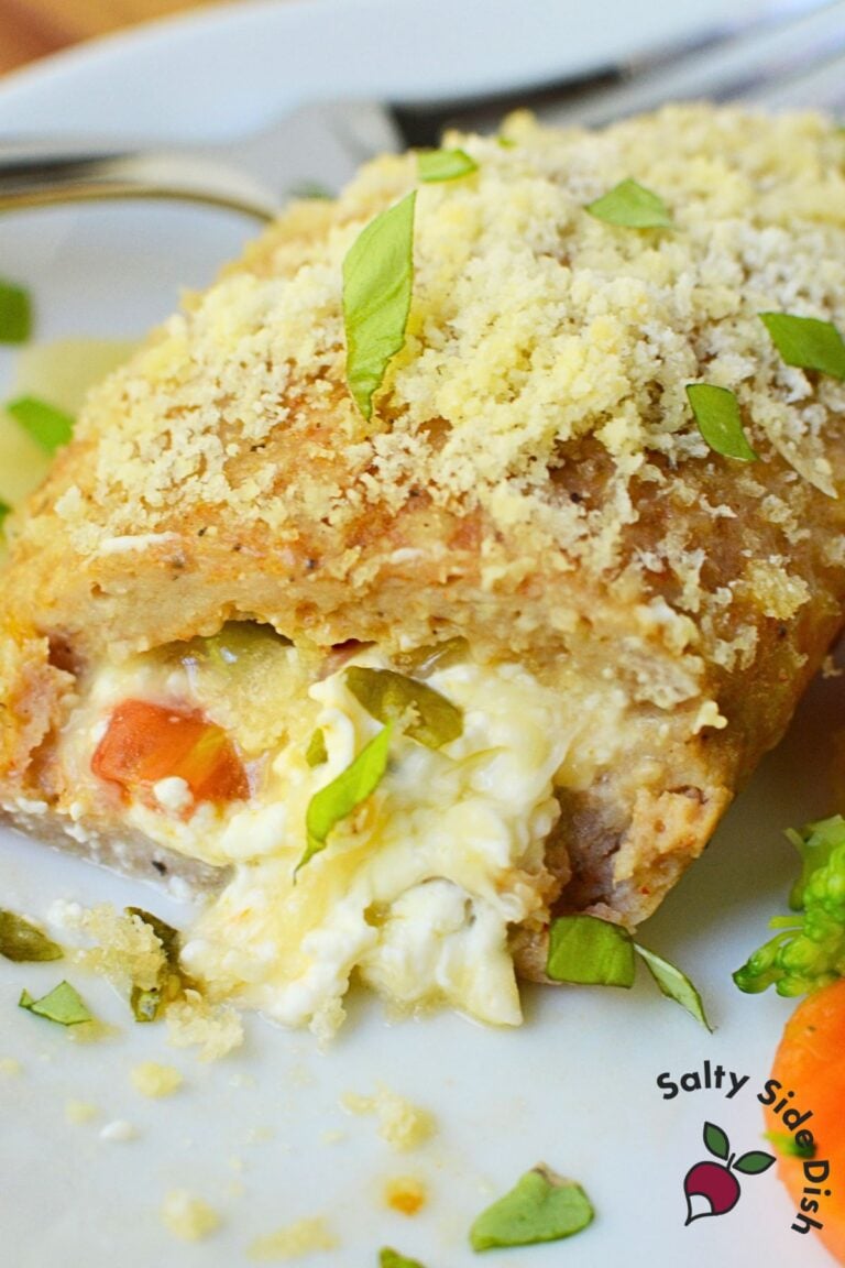 Sliced baked chicken pocket on a white plate showing cream cheese, tomato, and basil filling with a parmesan panko crust