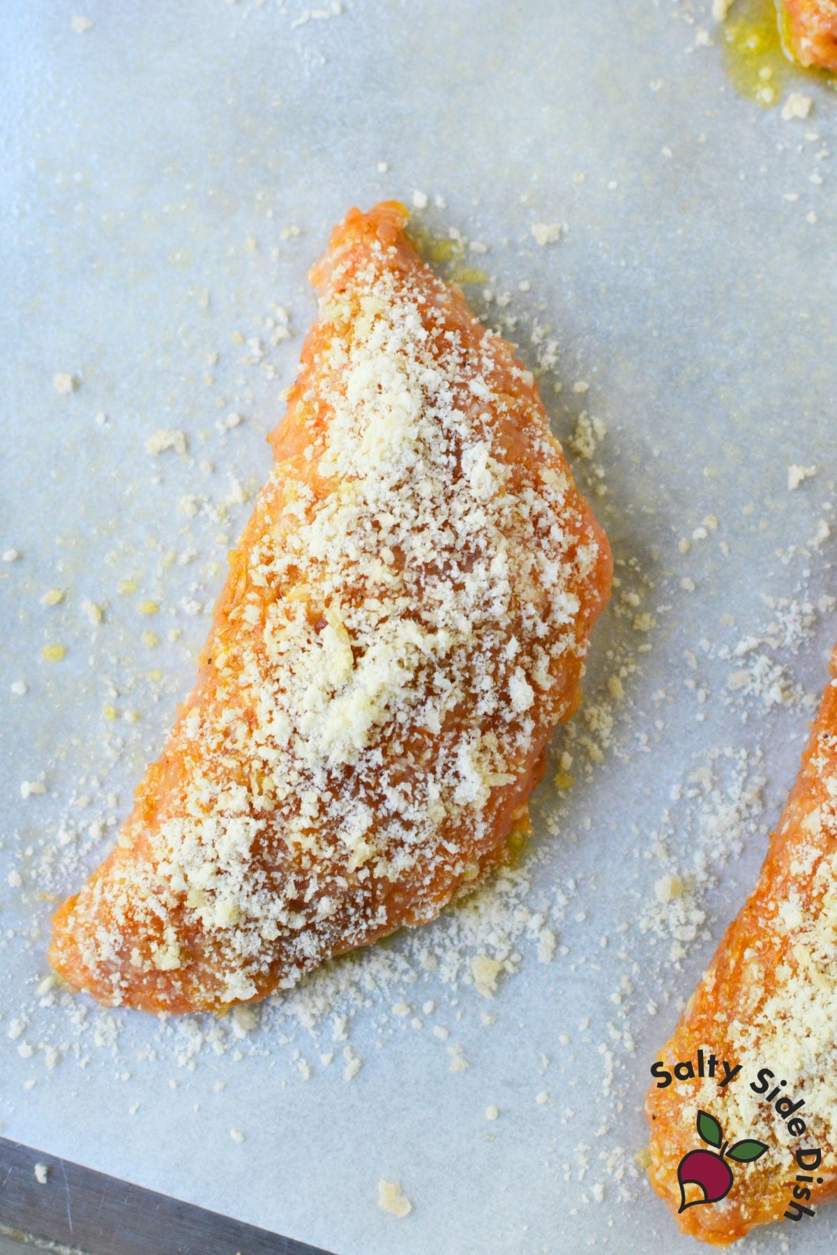 Raw chicken pocket coated in parmesan panko crumble on a parchment lined baking sheet