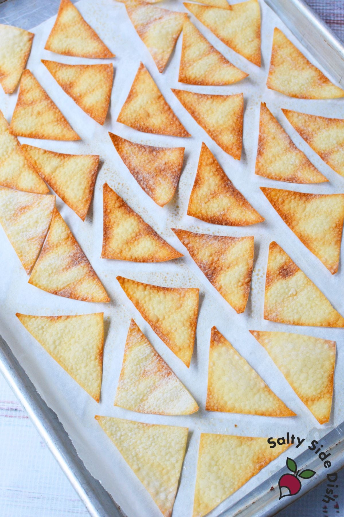 Baked wonton chip triangles cooling on a parchment lined baking sheet