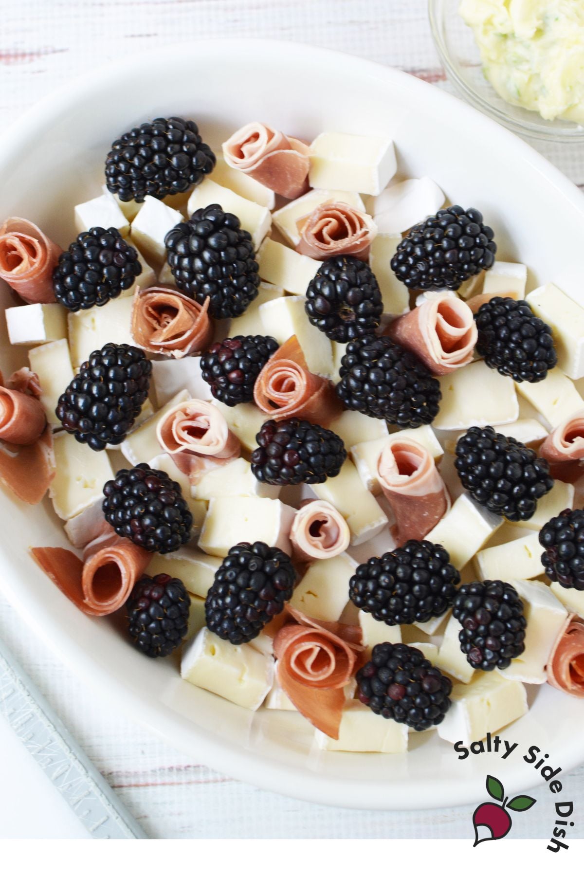 Cubed brie cheese topped with prosciutto rosettes and fresh blackberries before baking