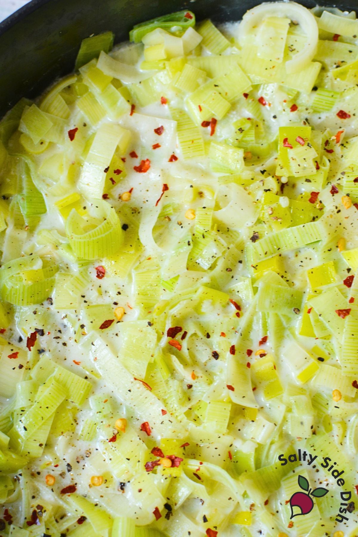 Bowl of creamed leeks garnished with red pepper flakes and black pepper