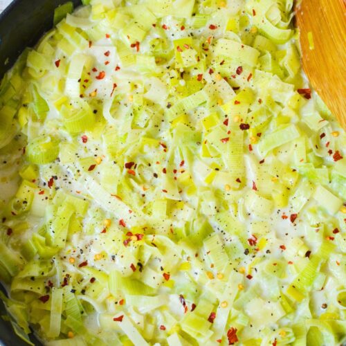 Creamy leeks in a skillet topped with red pepper flakes and black pepper