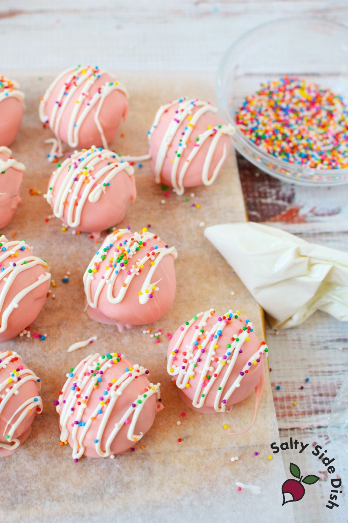 Decorating pink Oreo truffles with white candy drizzle and rainbow sprinkles