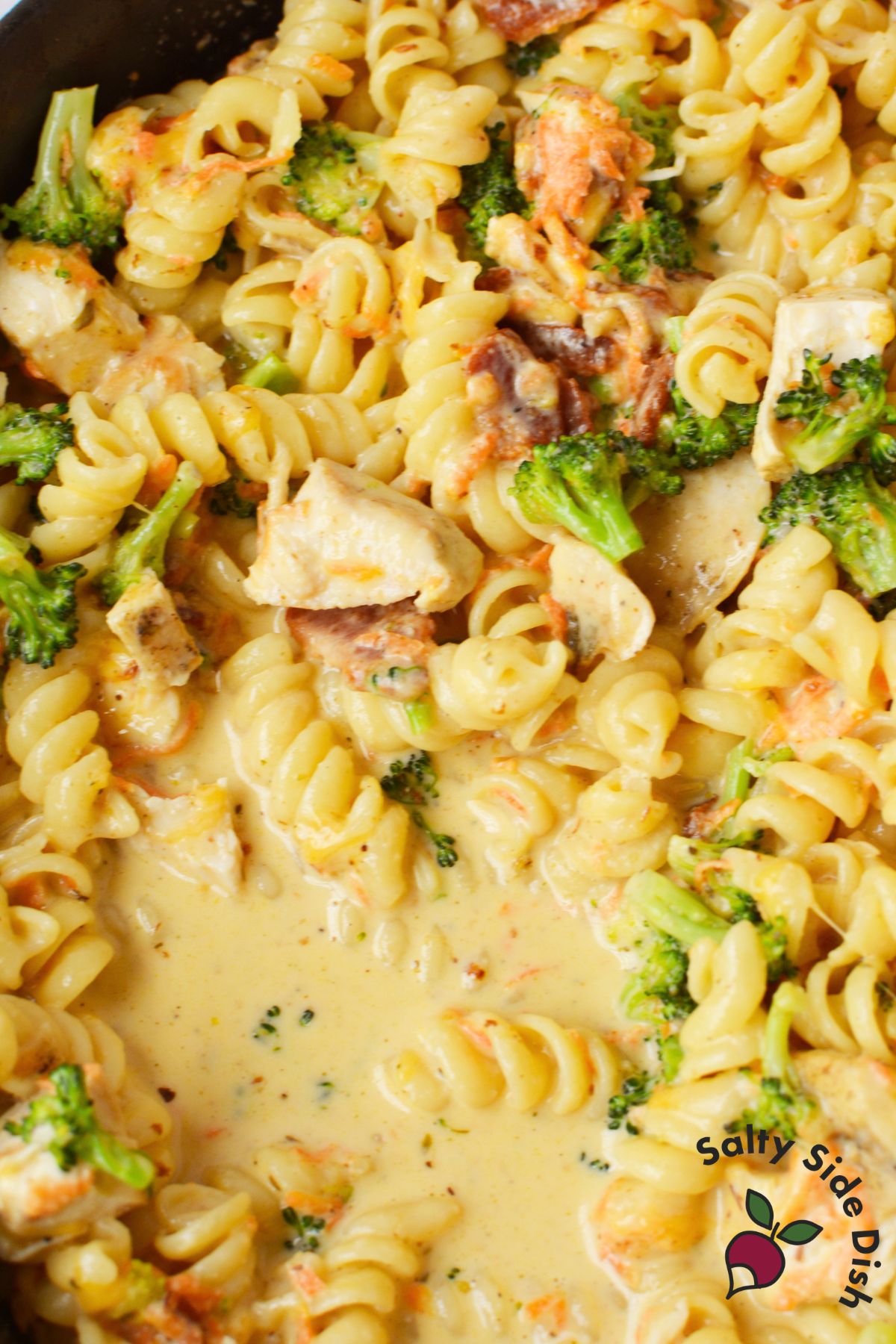 Creamy chicken bacon pasta with broccoli and carrots simmering in a cheesy sauce.