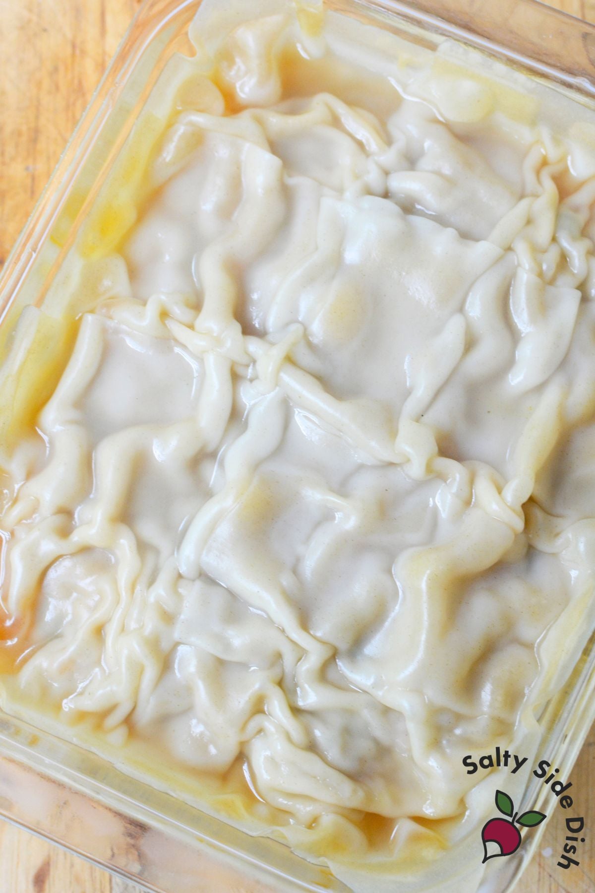 Uncooked dumpling lasagna layered with wonton wrappers in a glass baking dish.