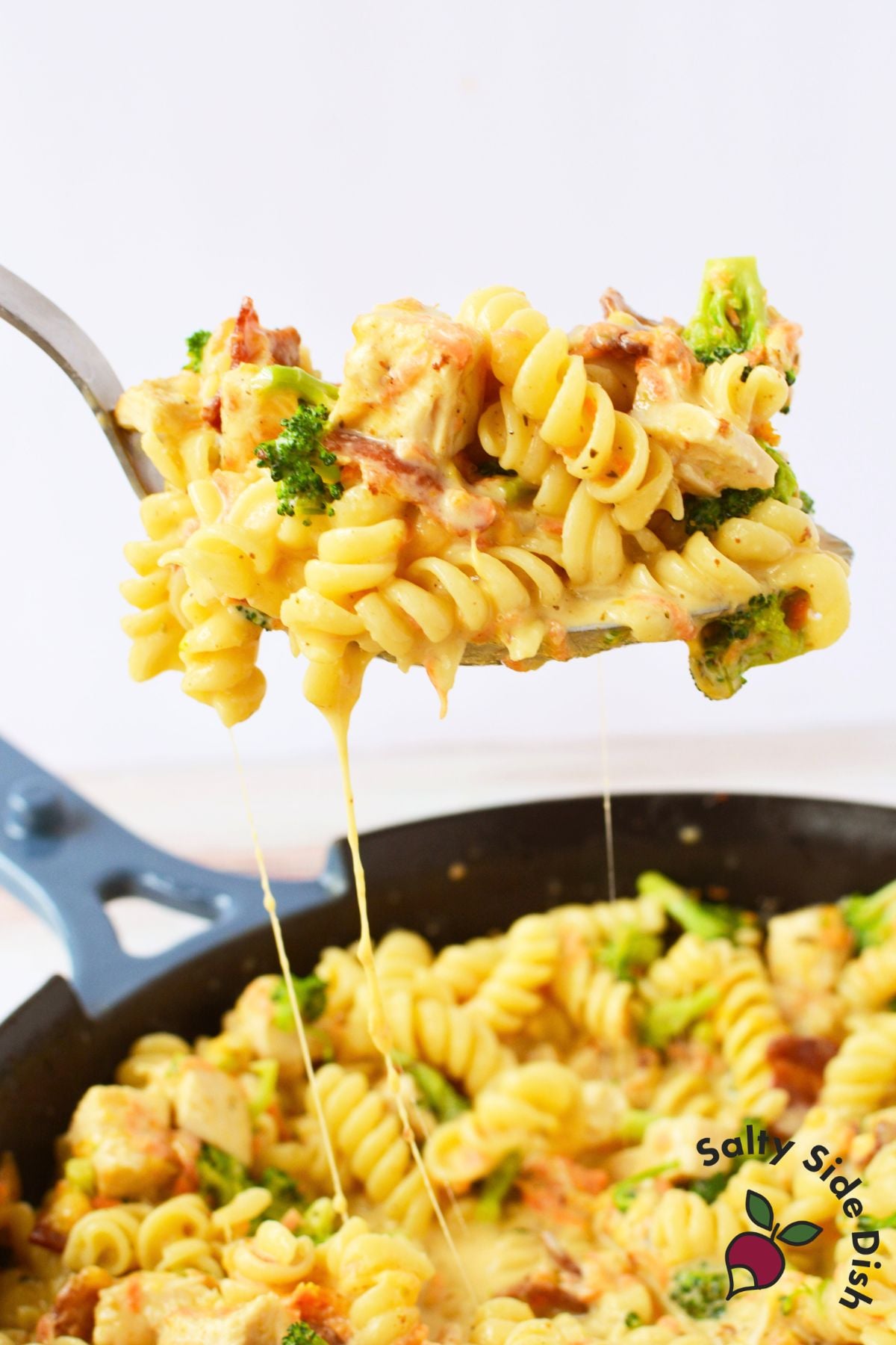 Spoonful of cheesy chicken bacon pasta with broccoli lifted above the skillet.