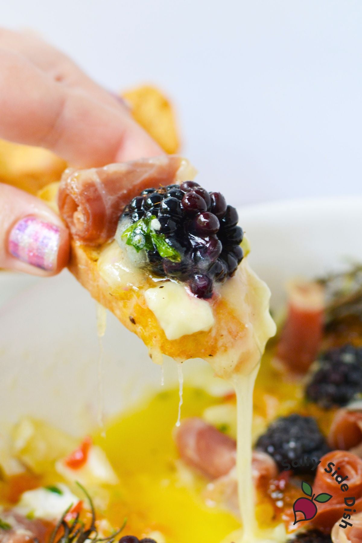 Melted cheese pulling into a string as a bite of charcuterie dip is lifted on bread