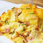 Plated slice of eggs benedict casserole with Canadian bacon and fresh chives
