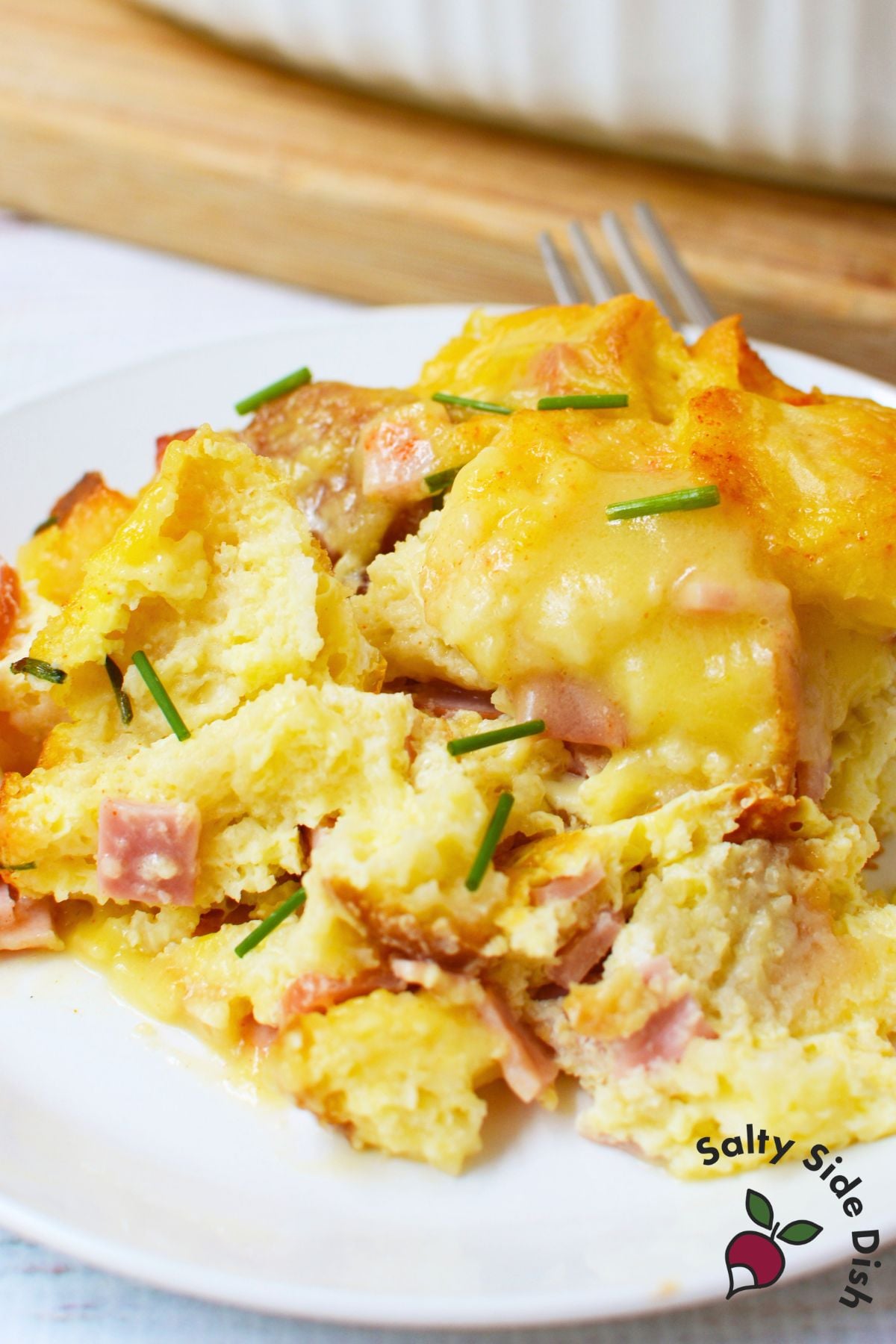 Plated slice of eggs benedict casserole with Canadian bacon and fresh chives