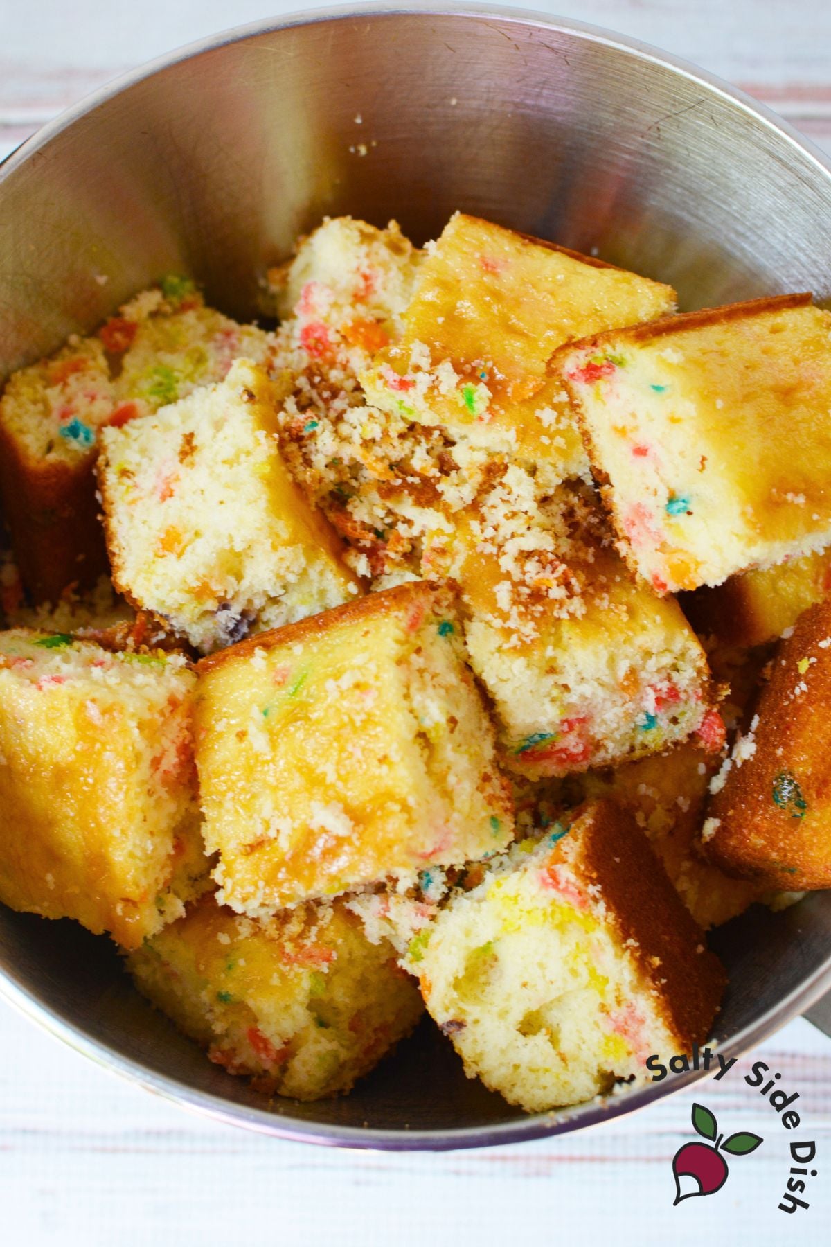 Baked fruity pebbles cake cut into cubes in a mixing bowl