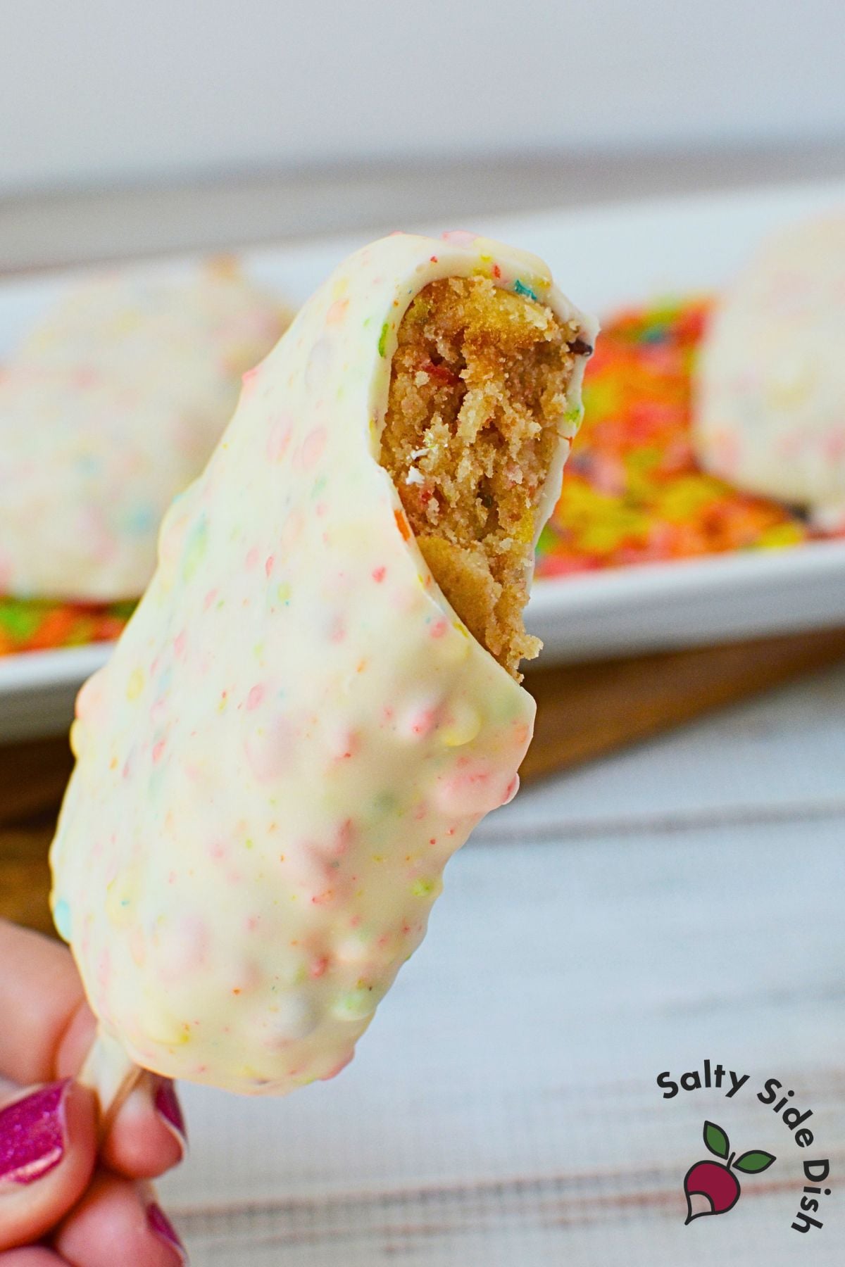 Fruity pebbles cake pop with a bite taken out showing the cake interior
