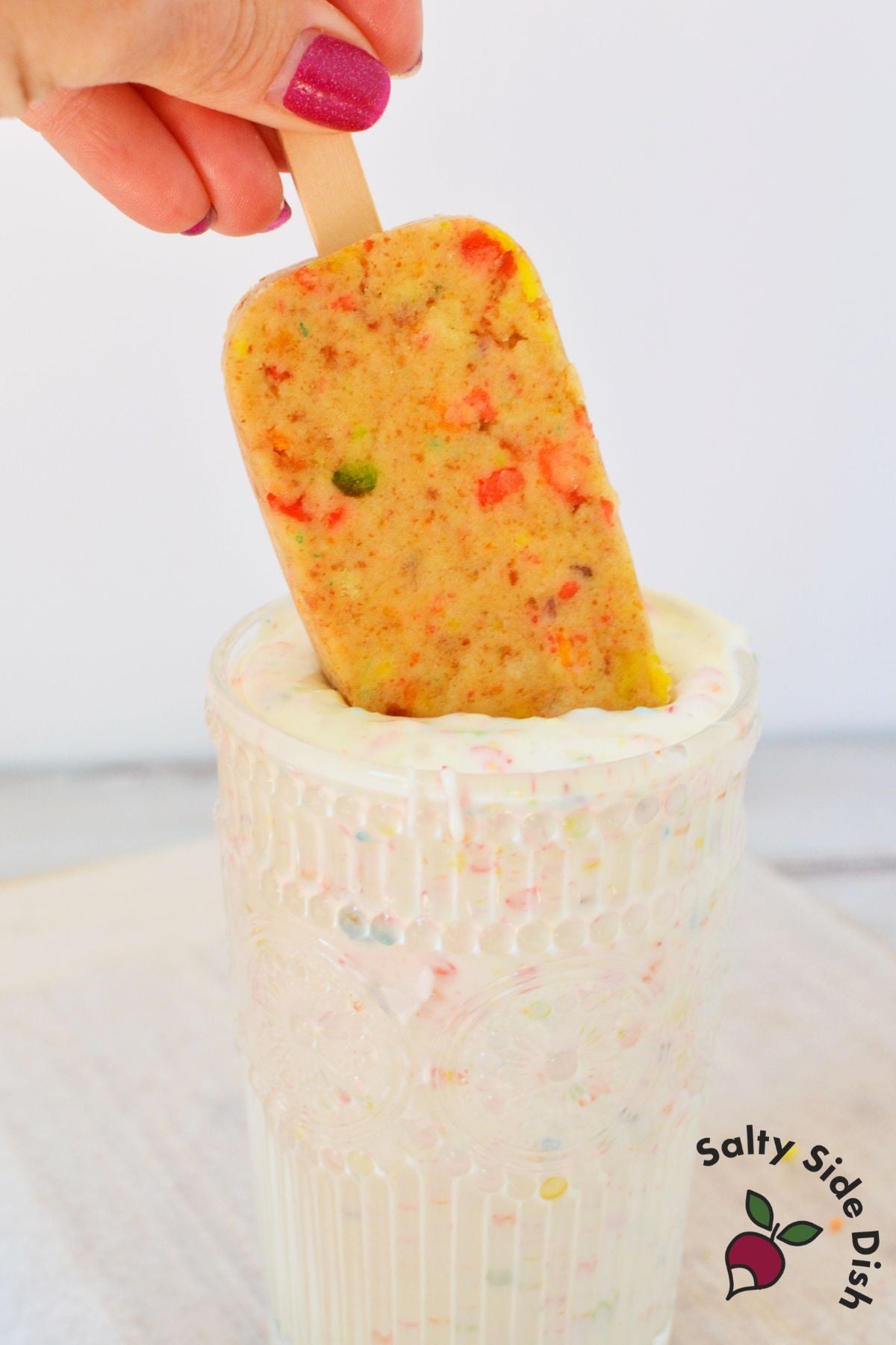 Fruity pebbles cake pop being dipped into white chocolate coating