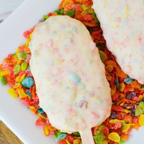 Two fruity pebbles cake pops on a plate lined with fruity pebbles cereal