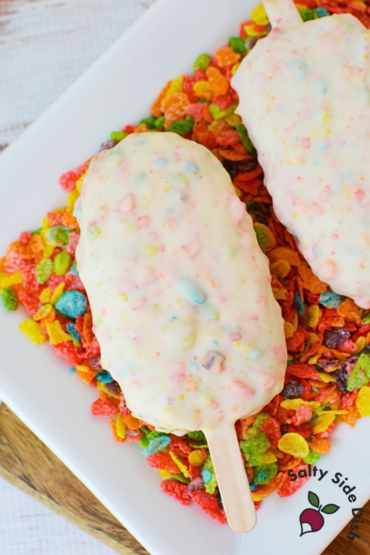 Two fruity pebbles cake pops on a plate lined with fruity pebbles cereal