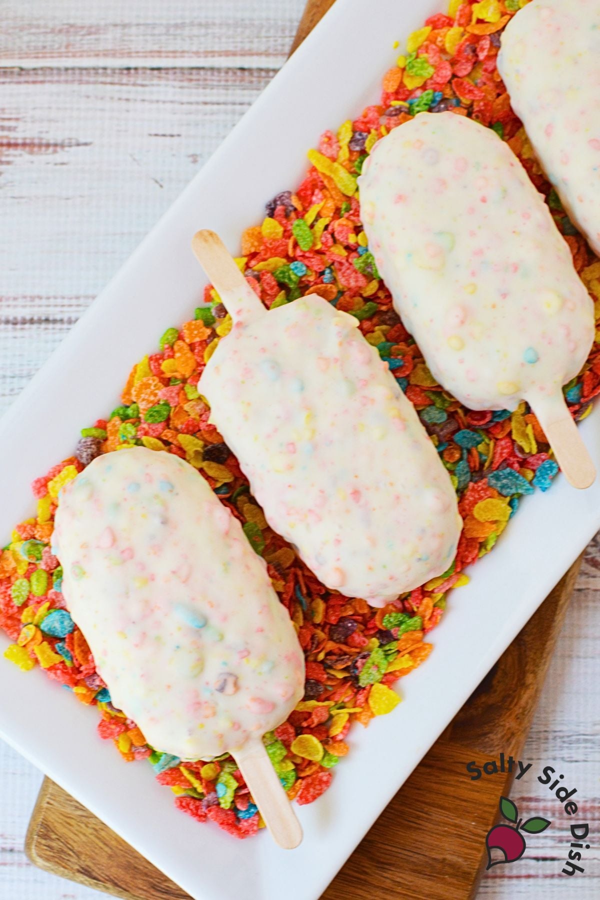 Three fruity pebbles cake pops arranged on a platter of fruity pebbles cereal