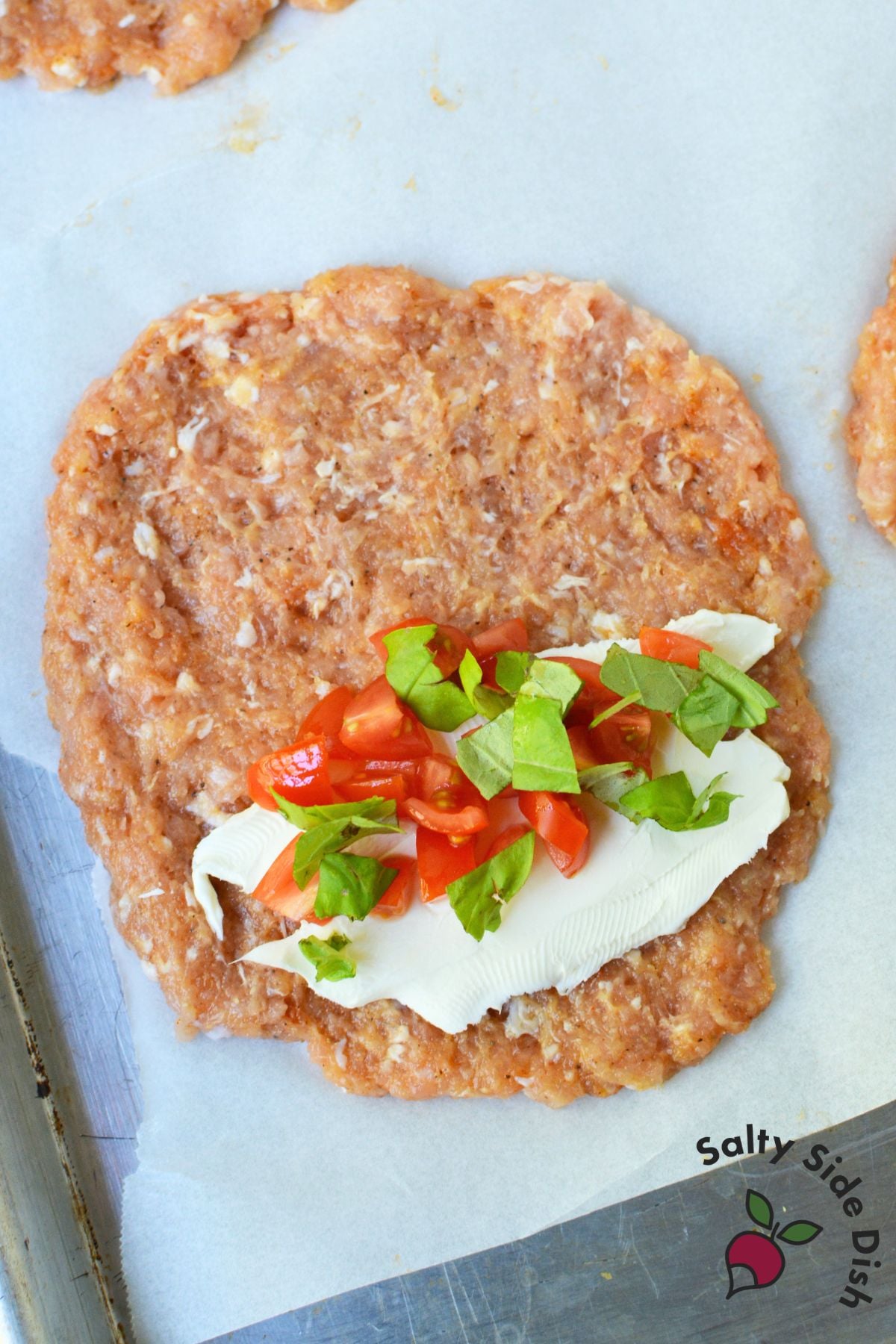 Ground chicken patty flattened on parchment paper before filling and folding
