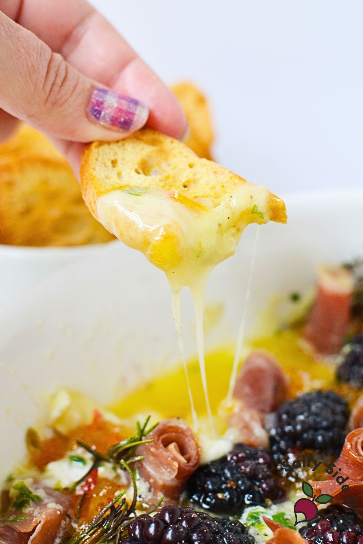 Toasted bread dipped into warm charcuterie dip with melted brie and blackberries
