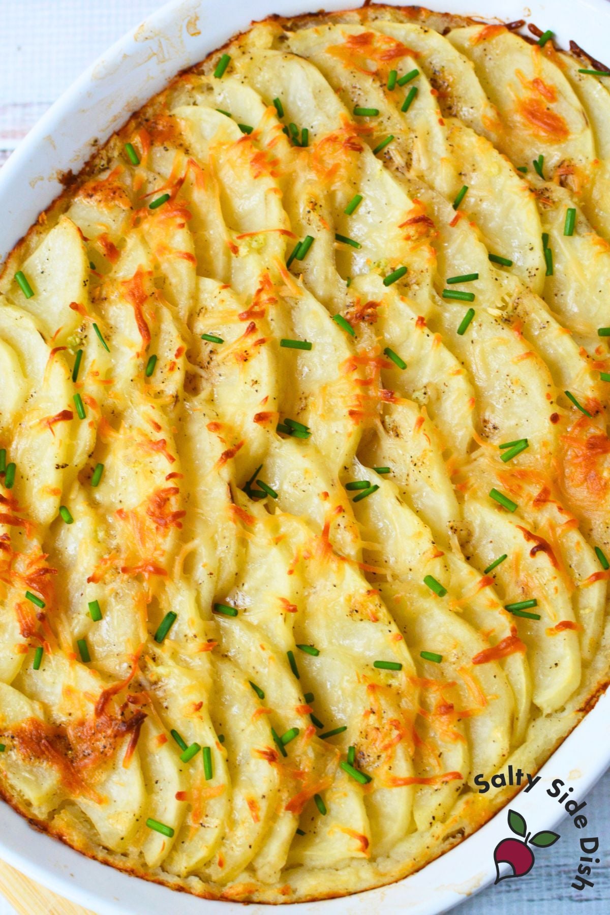 Baked potato gratin with browned cheese and chives in a white dish