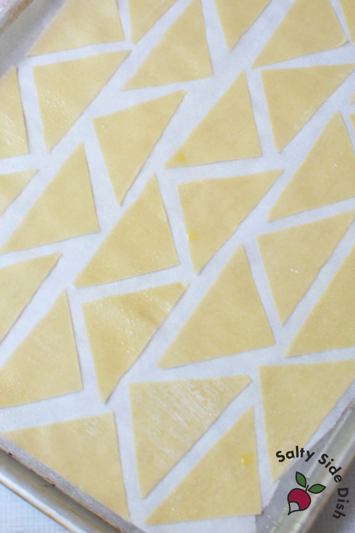 Wonton wrappers cut into triangles on a parchment lined baking sheet before baking
