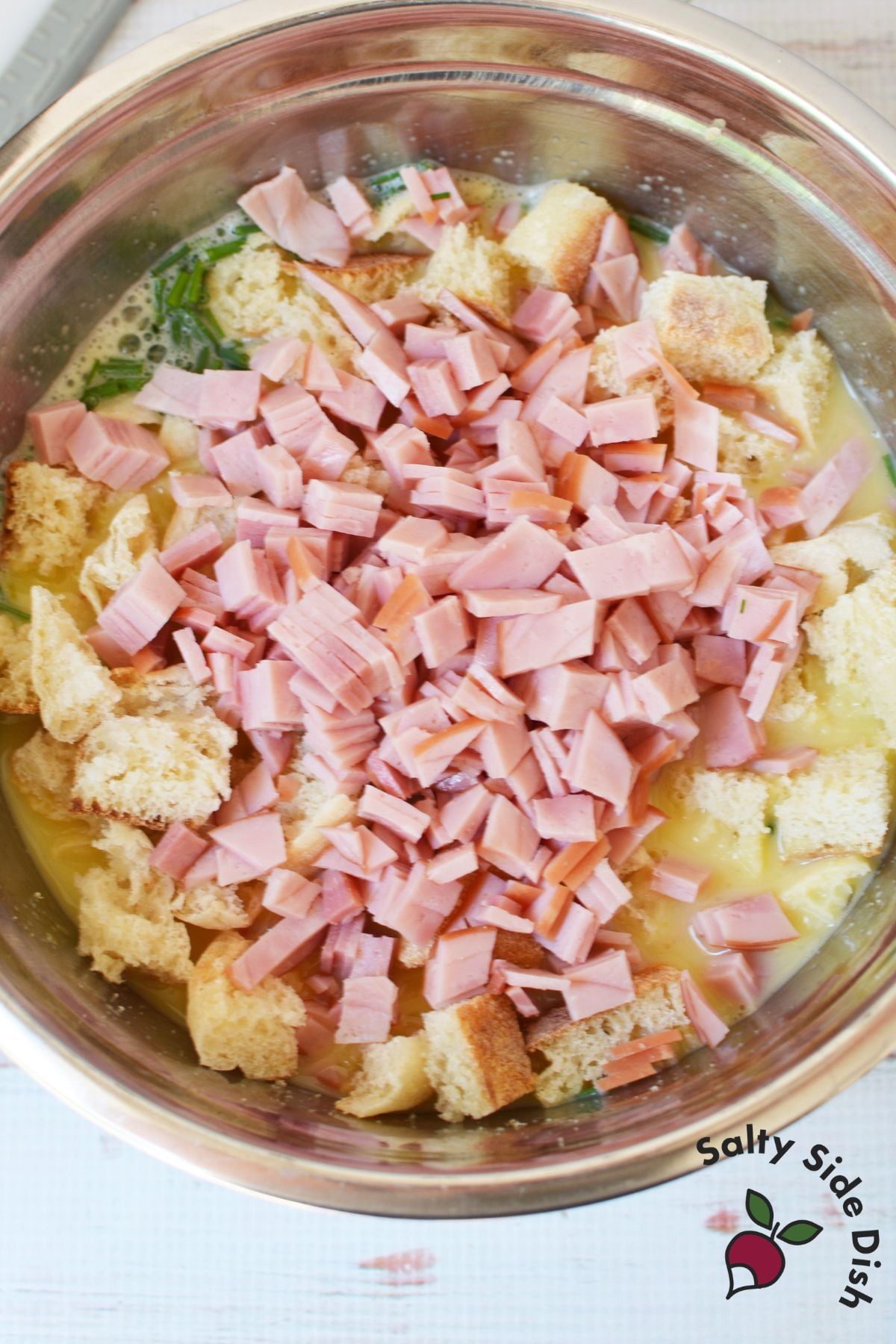 Cubed English muffins and diced Canadian bacon mixed into egg custard in a bowl