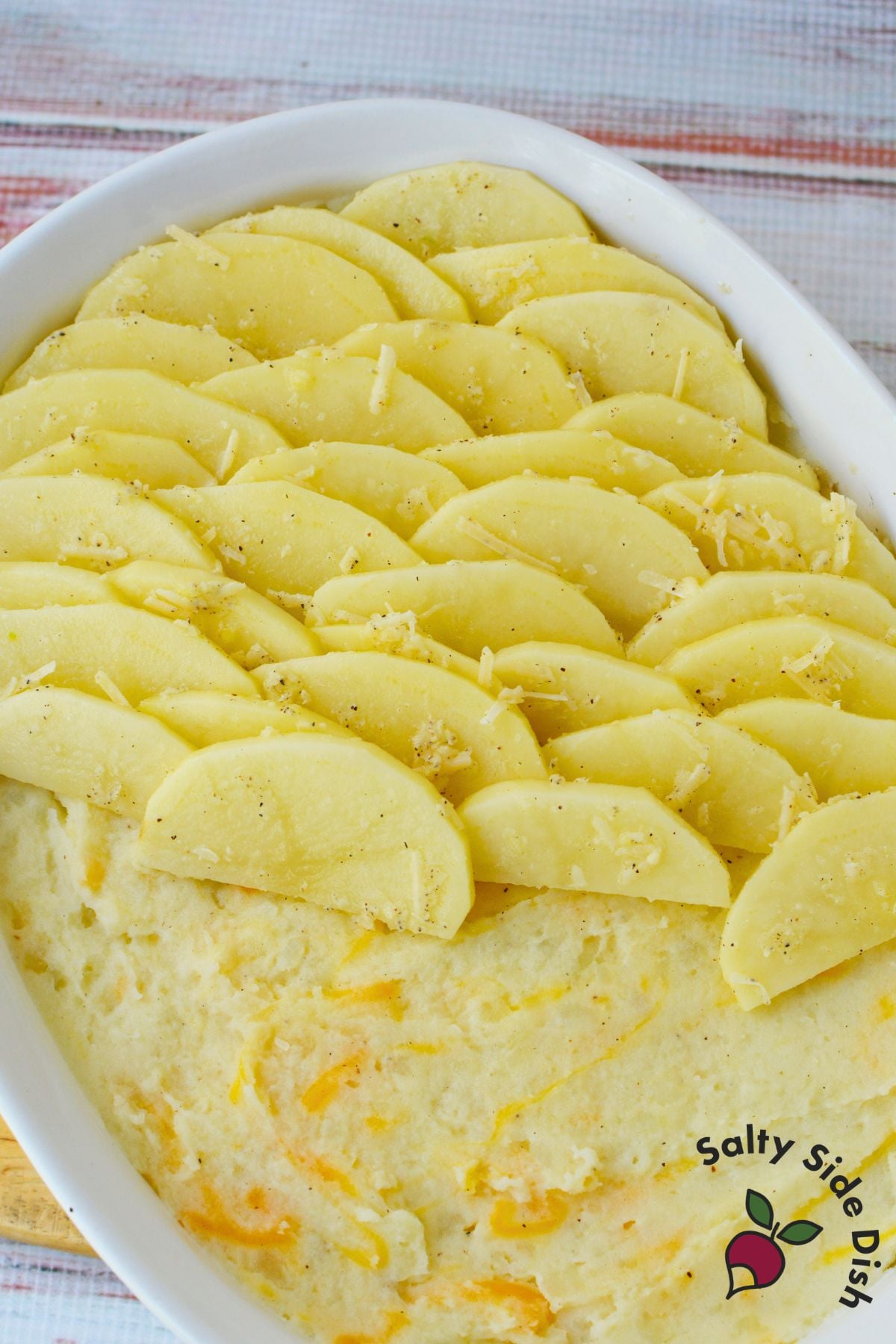 Sliced potatoes layered over mashed potatoes in a baking dish before baking