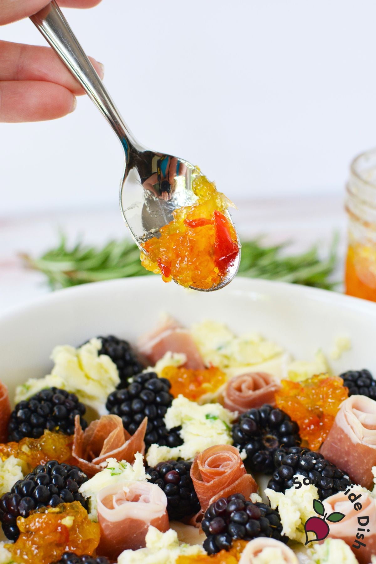 Spoonful of hot pepper jelly being added to charcuterie dip with prosciutto and blackberries