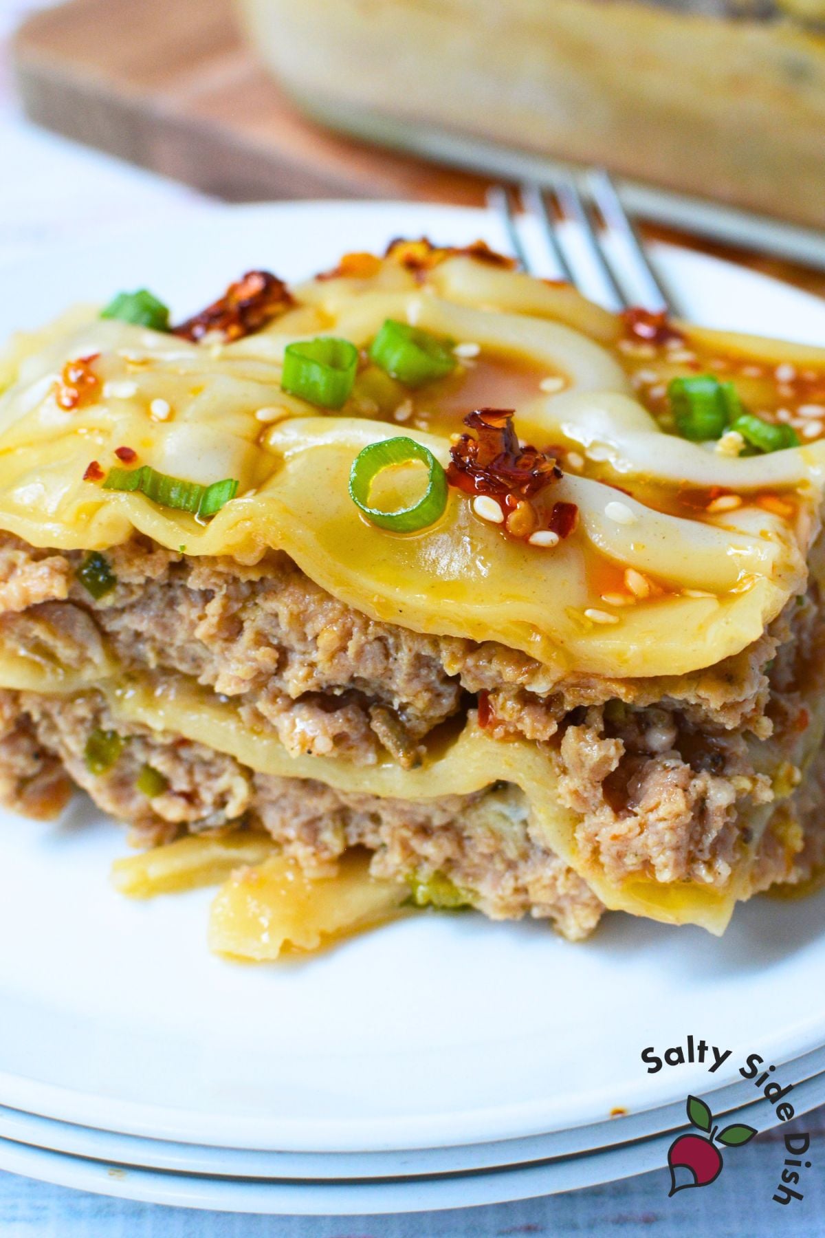 Close-up slice of layered pork dumpling lasagna with green onions, sesame seeds, and chili oilClose-up slice of layered pork dumpling lasagna with green onions, sesame seeds, and chili oil.