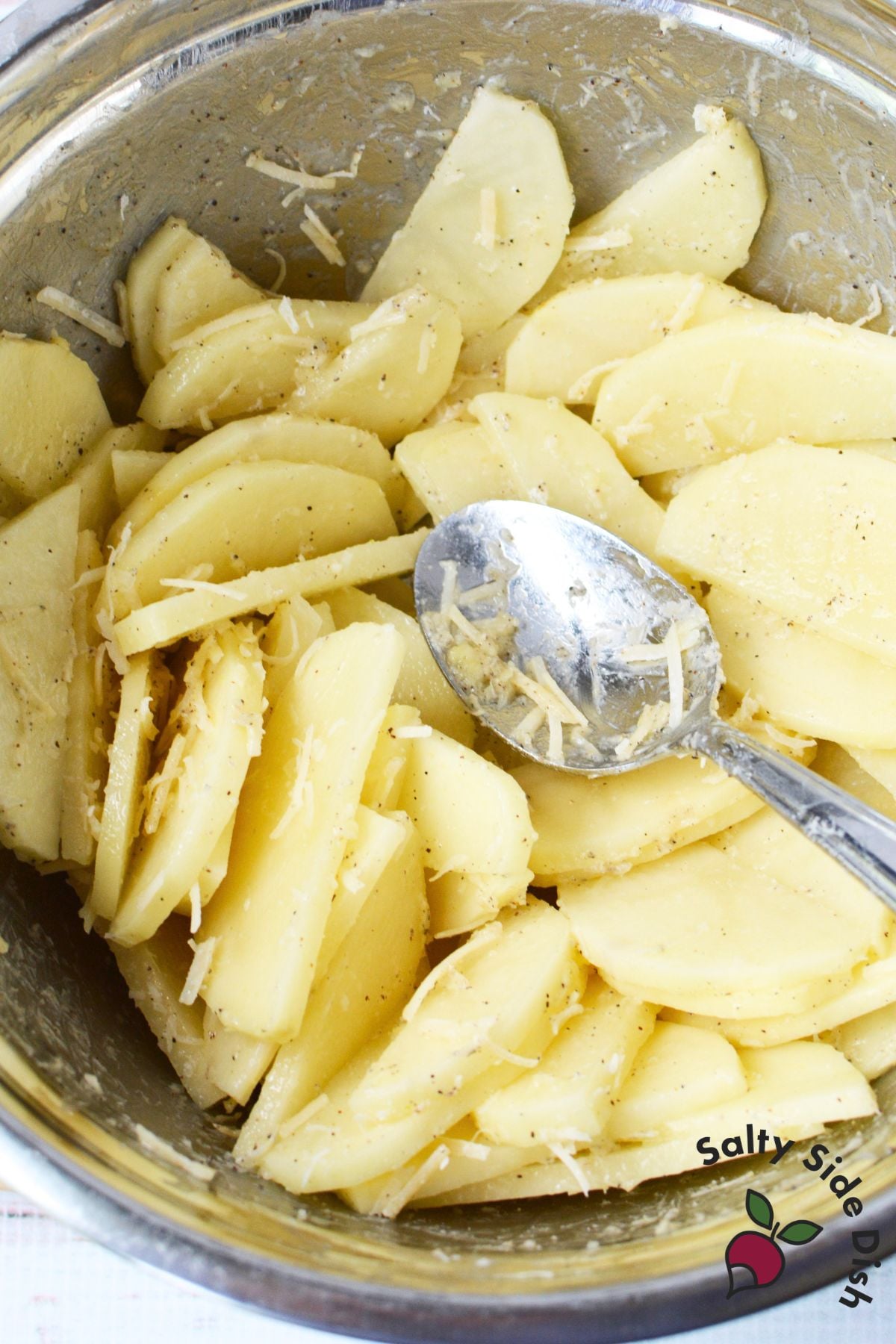 Sliced potatoes mixed with Parmesan, garlic, and pepper in a bowl
