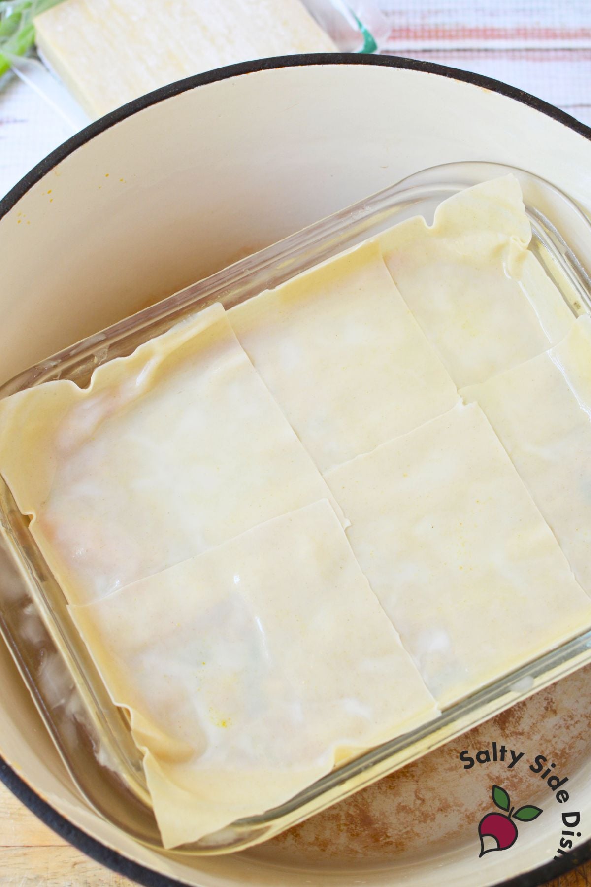 Glass baking dish filled with layered wonton wrappers set inside a large pot for steaming.