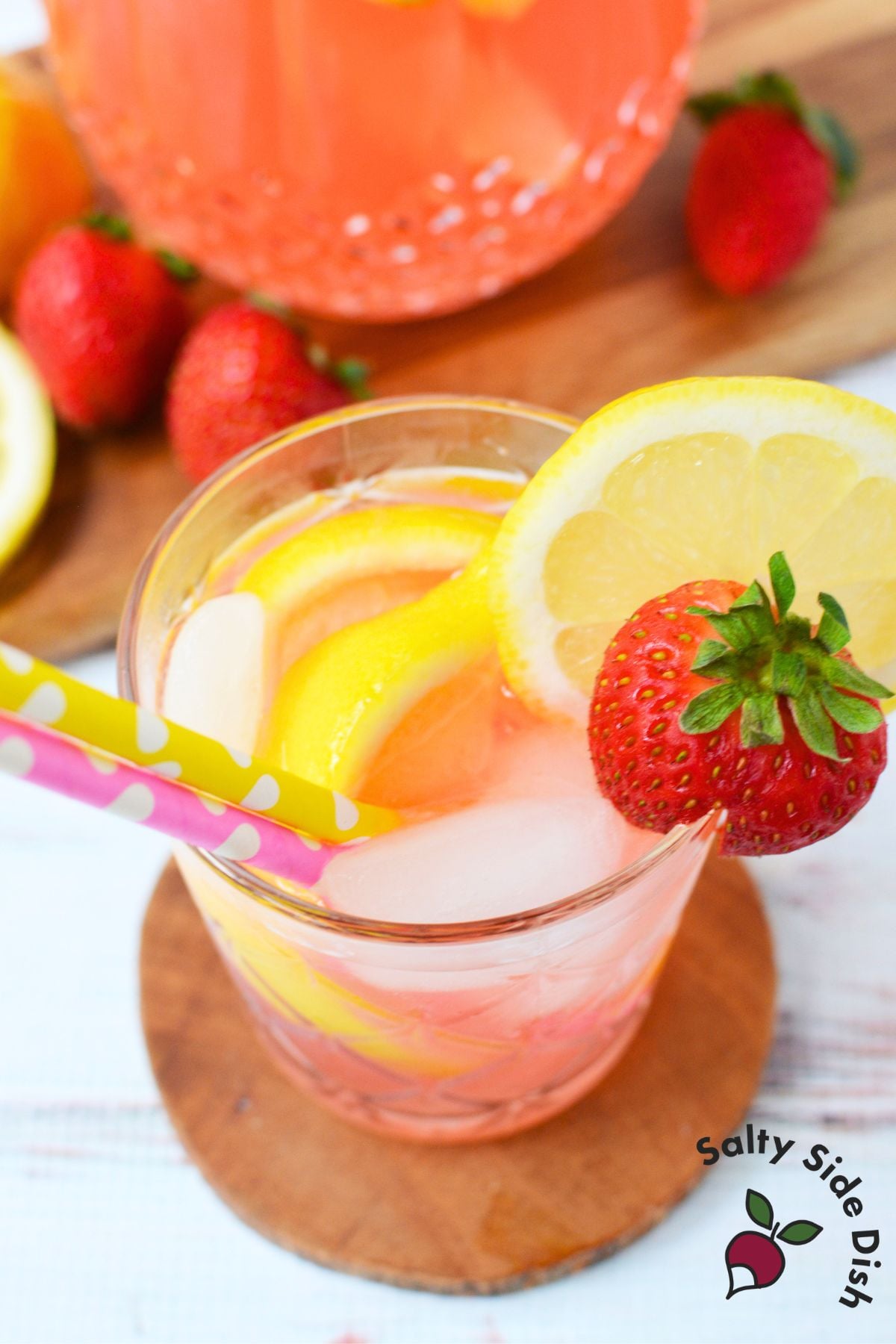 Tablespoon of strawberry syrup being added to a pitcher of lemonade