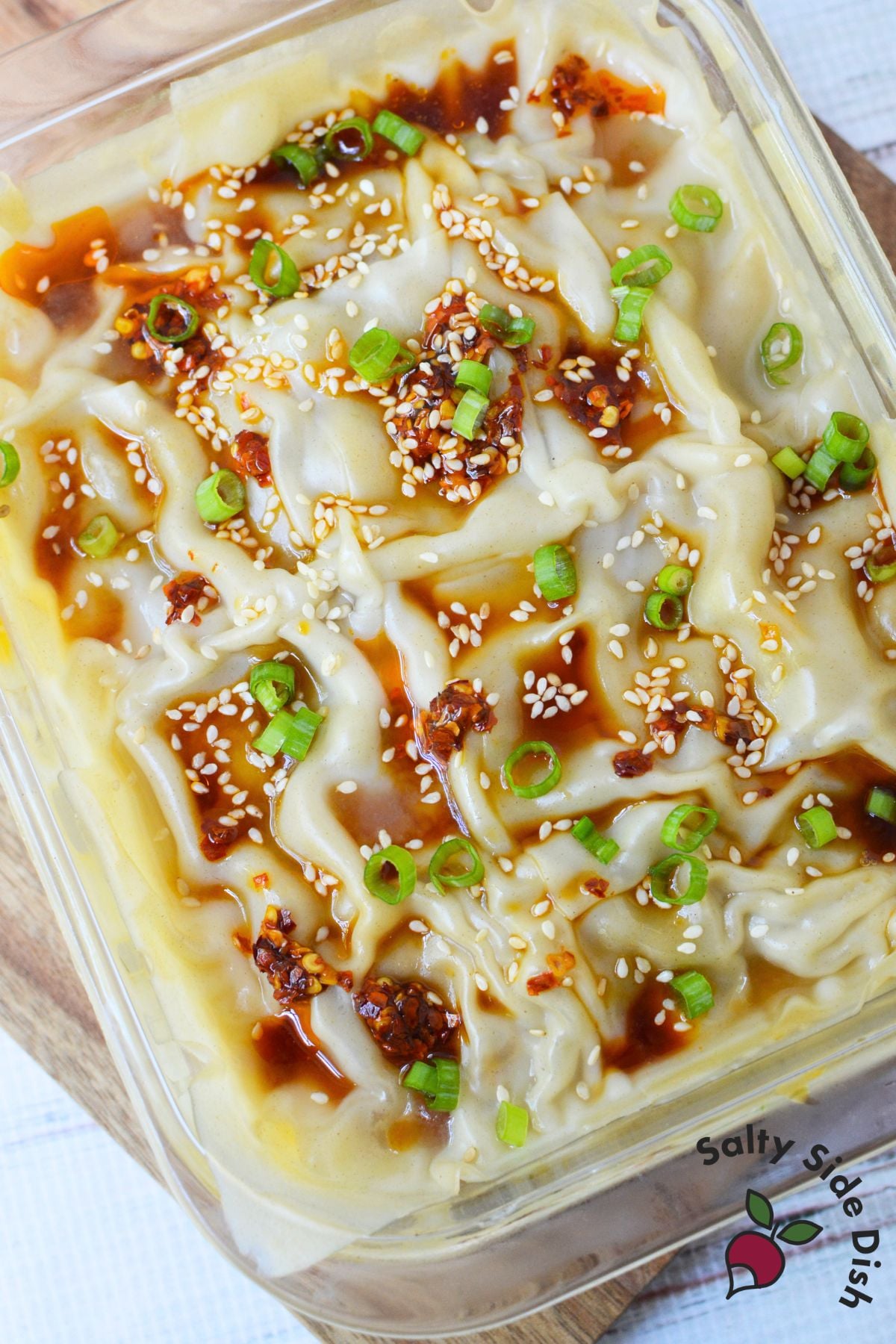 Finished dumpling lasagna in a glass baking dish topped with chili oil, sesame seeds, soy sauce, and sliced green onions.
