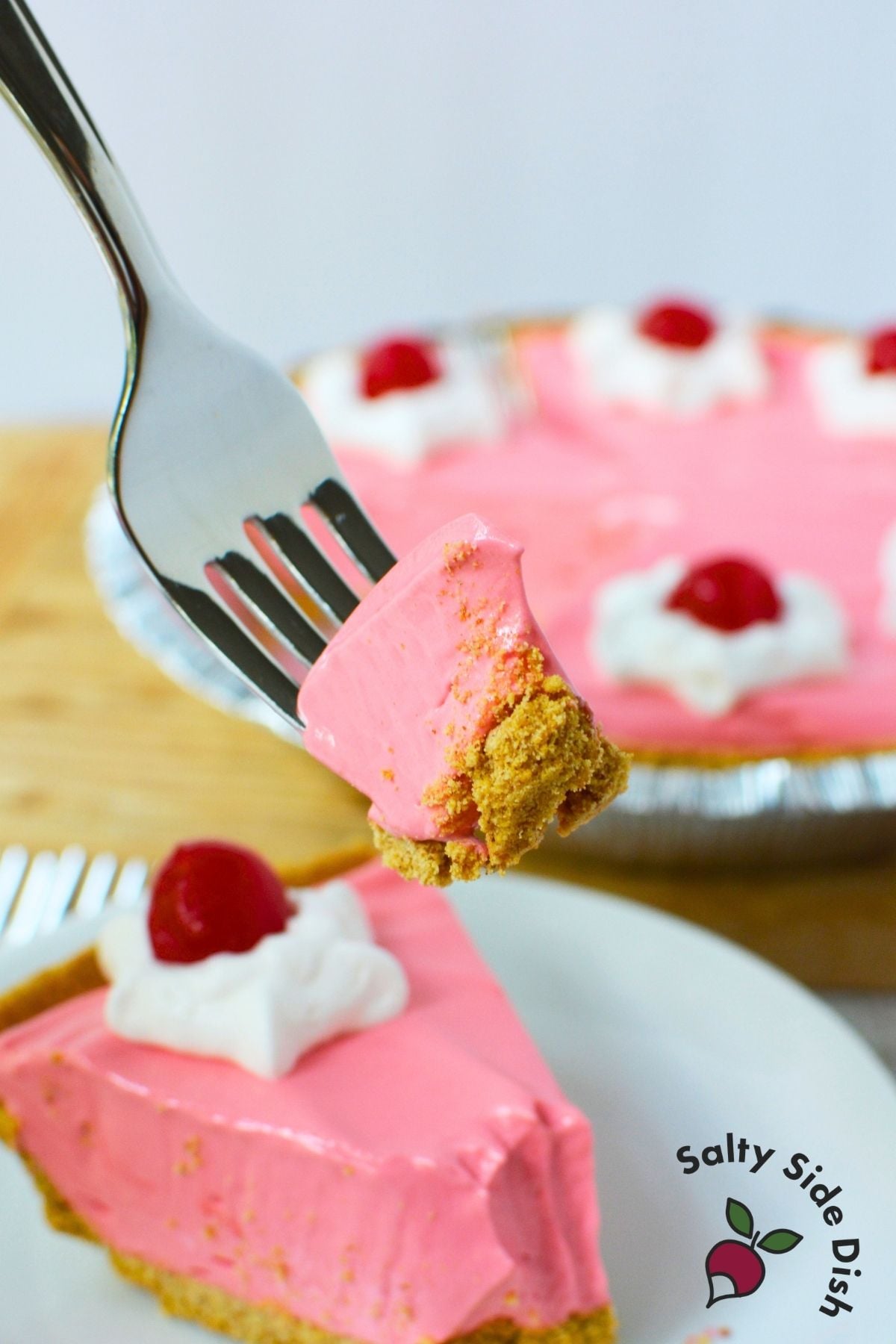 Bite of cherry Kool Aid pie on a fork with graham cracker crust and creamy pink filling