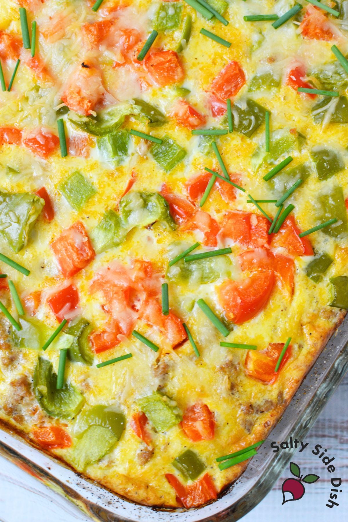Close up of baked breakfast potato casserole with melted cheese, bell peppers and chives