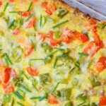 Close up of baked breakfast potato casserole with melted cheese, bell peppers and chives