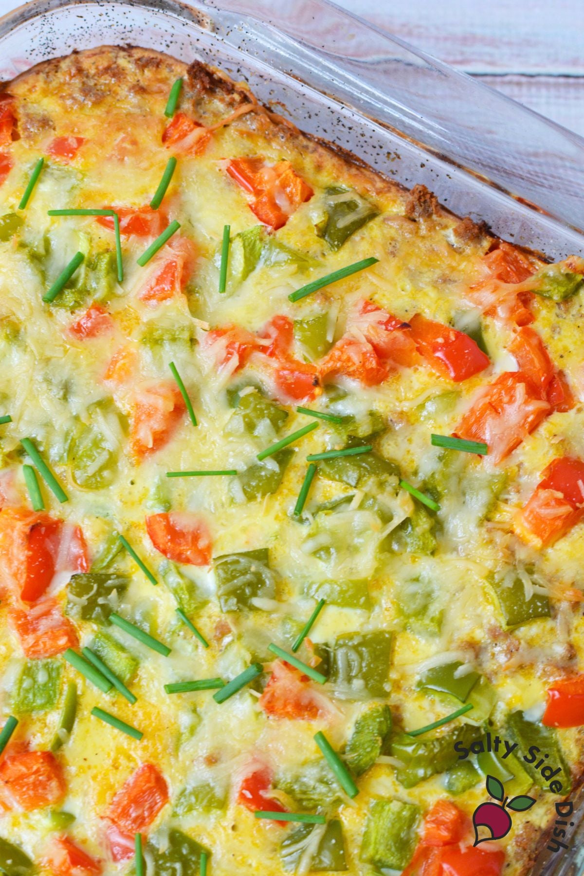 Close up of baked breakfast potato casserole with melted cheese, bell peppers and chives
